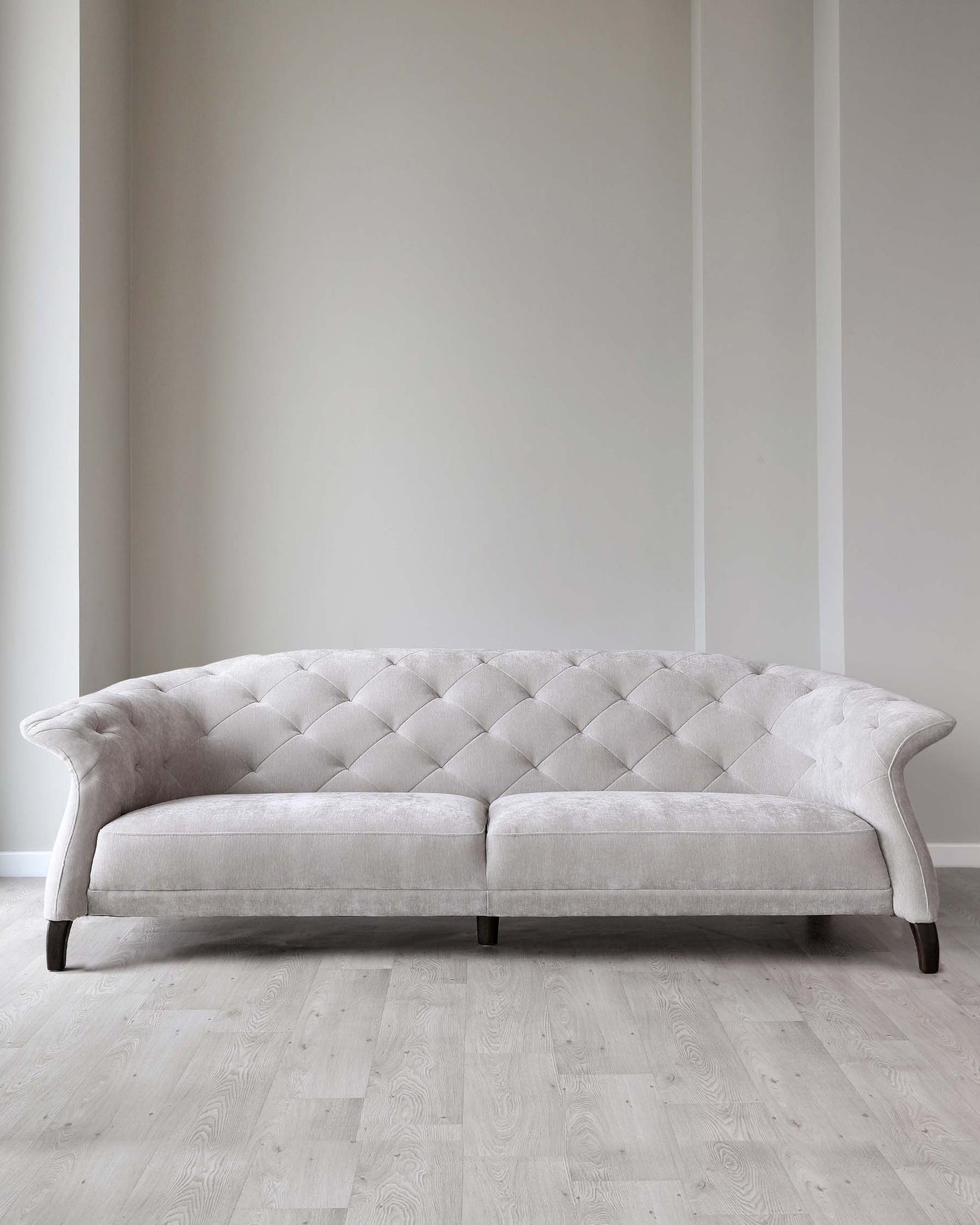 Elegant light grey tufted fabric sofa with curved armrests and dark wooden legs set against a neutral-toned wall and light hardwood floor.