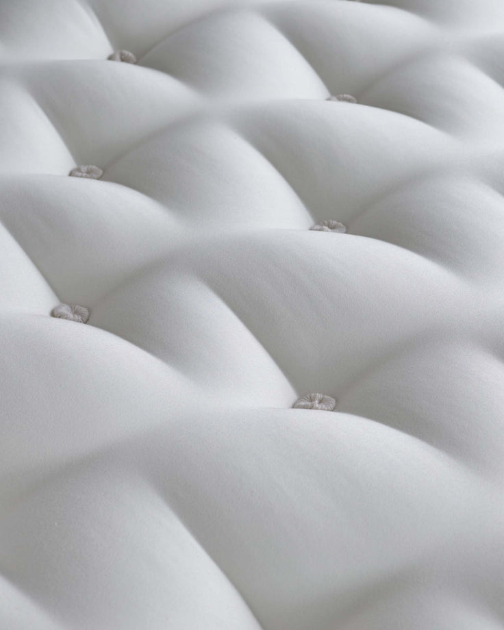 Close-up view of a tufted white upholstered headboard or cushion with diamond pattern stitching and button details