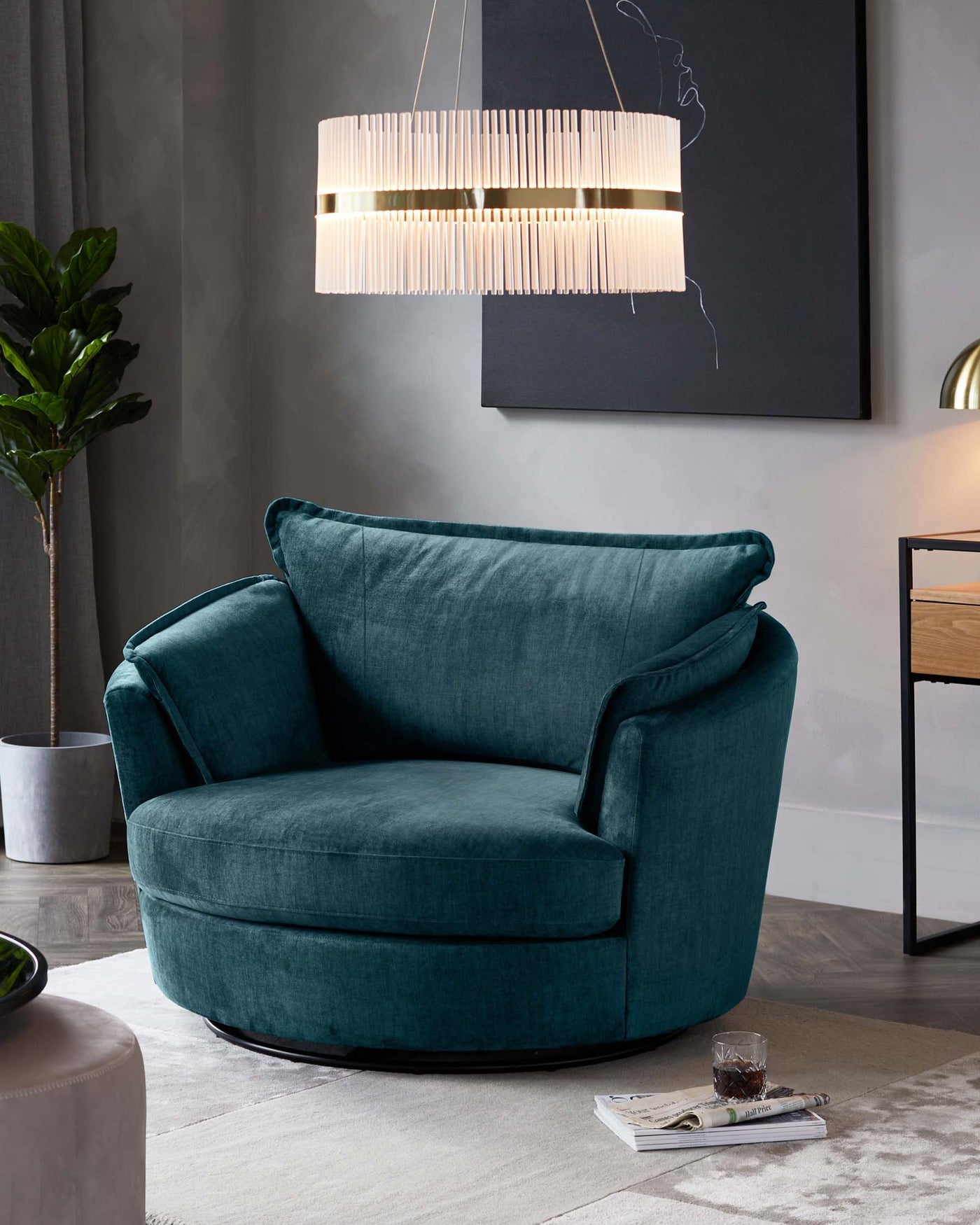 Luxurious deep teal velvet swivel chair with plush curved backrest and large rounded seat cushion. An adjacent sleek wood and metal side table with minimalistic design complements the chair. Elegant cylindrical pendant light with vertical slats hangs above, casting a soft glow. The setting includes a grey textured rug, a potted green plant to the left, and hints of a contemporary art piece in the background, creating a sophisticated ambiance.