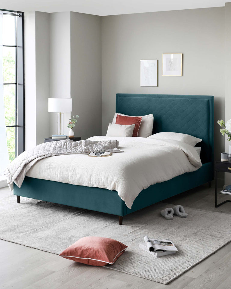 Elegant bedroom furniture comprising a plush teal upholstered king-sized bed with a tufted headboard, flanked by a sleek, dark wood nightstand with an open shelf and single drawer. The nightstand is accessorized with a contemporary white table lamp with a cylindrical shade. A complementary light grey area rug is laid out beneath the bed, adding texture to the room.
