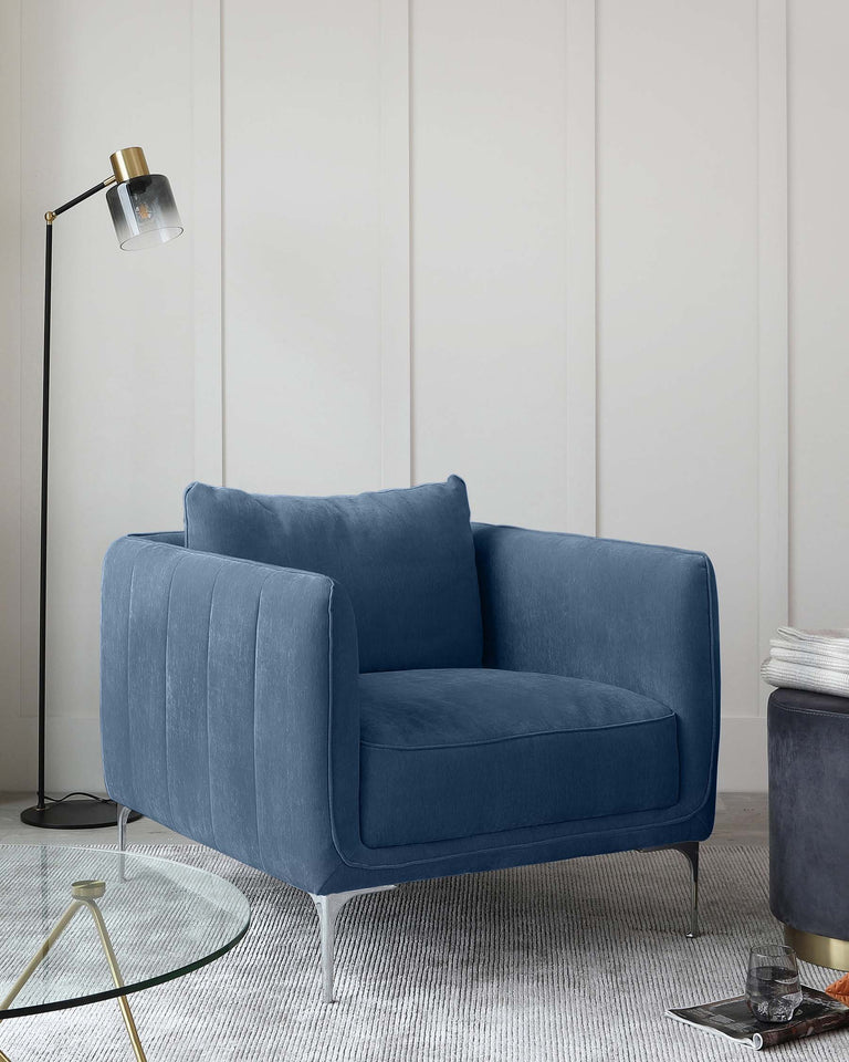 Elegant modern blue velvet armchair with sleek metal legs, beside a standing lamp with a black base and golden accents, over a textured woven rug in a chic interior setting with white panelled walls.