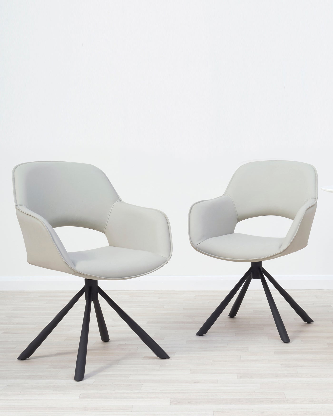 Two modern light grey upholstered accent chairs with black four-pointed star base, placed on a light hardwood floor against a white wall.