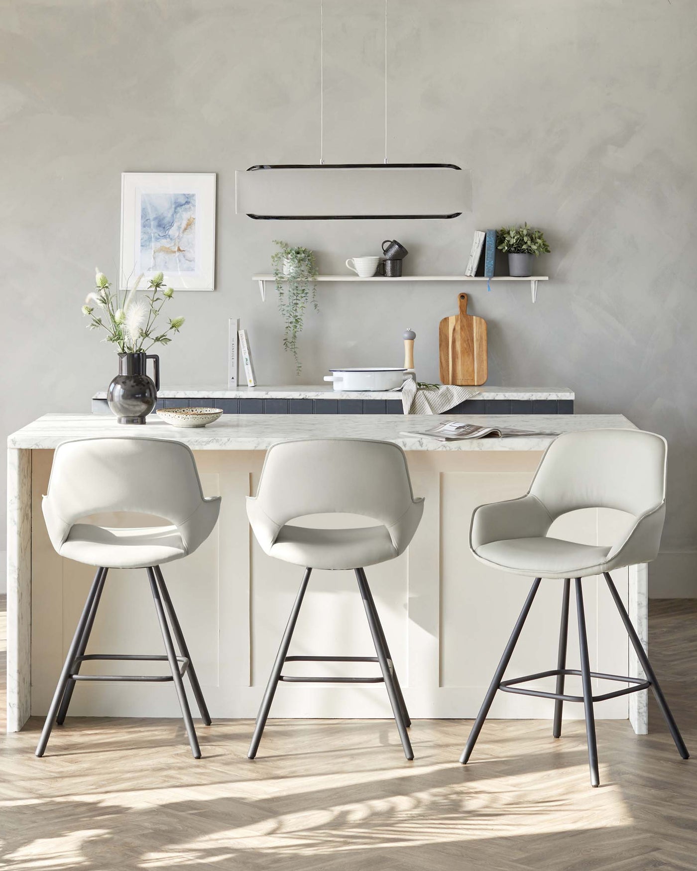 Three modern bar stools with beige upholstery and black metal legs positioned at a kitchen island with a marble countertop.