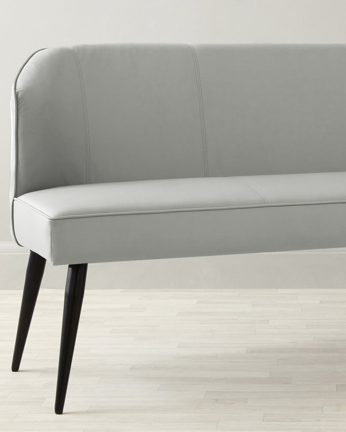 Contemporary light grey upholstered bench with a streamlined design, featuring a high curved backrest with accent stitching and four angled black wooden legs.
