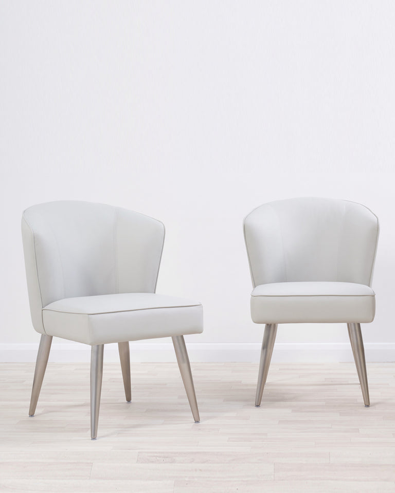 Two contemporary light grey upholstered armchairs with angled wooden legs set against a neutral backdrop.