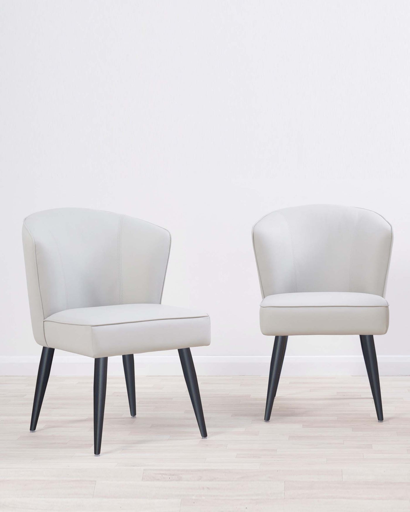 Two modern mid-century accent chairs with light grey upholstery and angled black wooden legs.