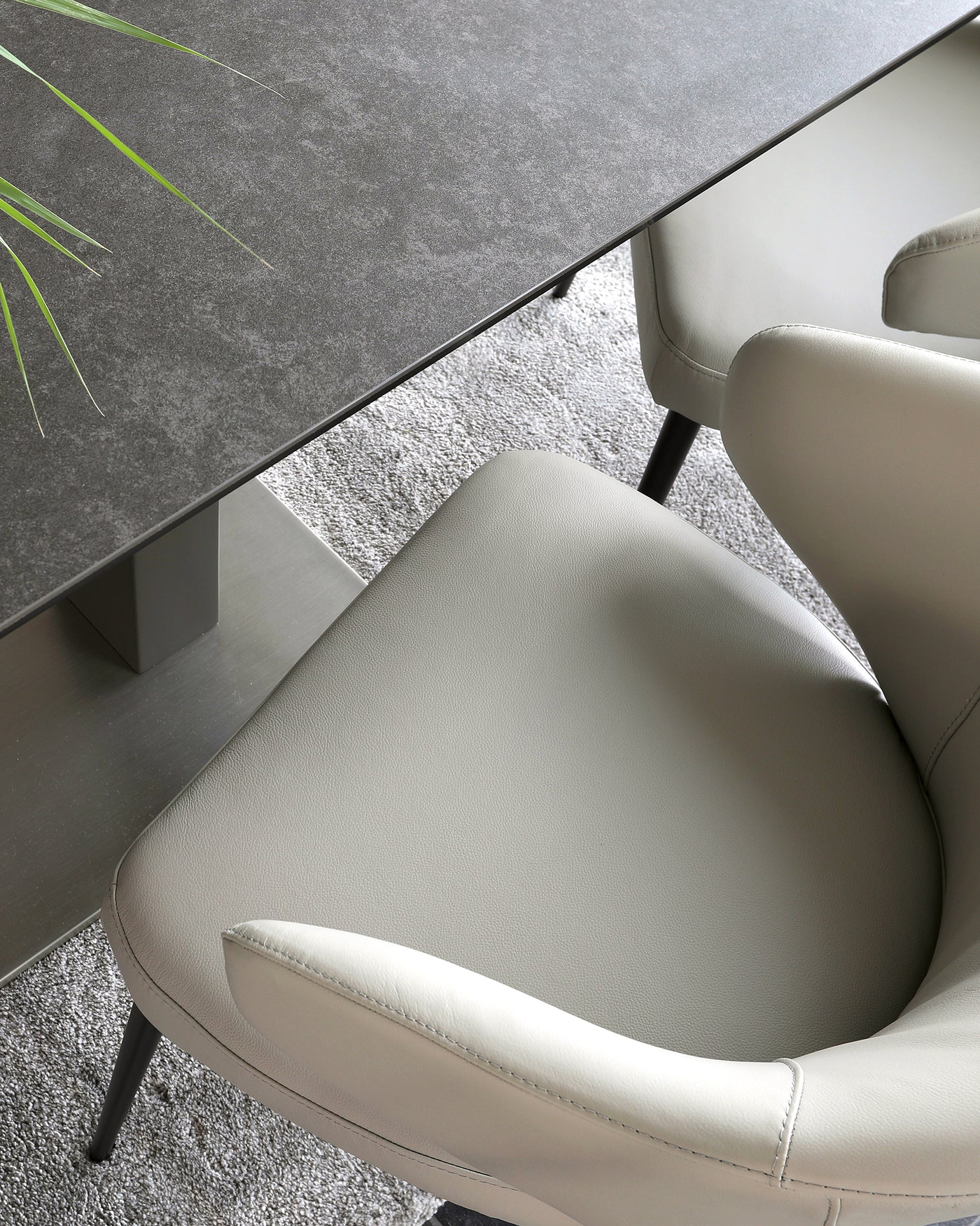 Modern stone grey dining table with sleek metallic legs paired with elegant light grey upholstered dining chairs featuring a curved backrest and black metallic legs. The setting is complemented by a plush grey area rug underneath.