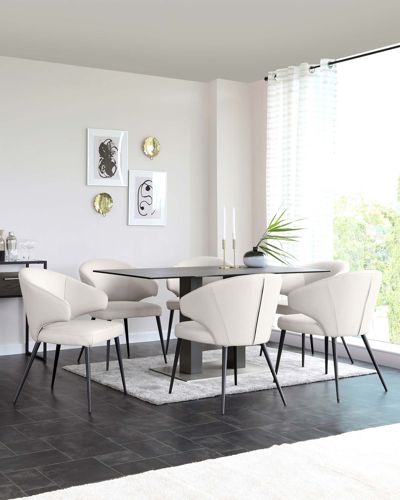 Modern dining room furniture set featuring an oval-shaped table with a matte black tabletop and a dark, sturdy base. Accompanied by four elegant, curved-back chairs upholstered in a light beige fabric with contrasting black metal legs. A plush white rug underlays the setup on a dark tiled floor.