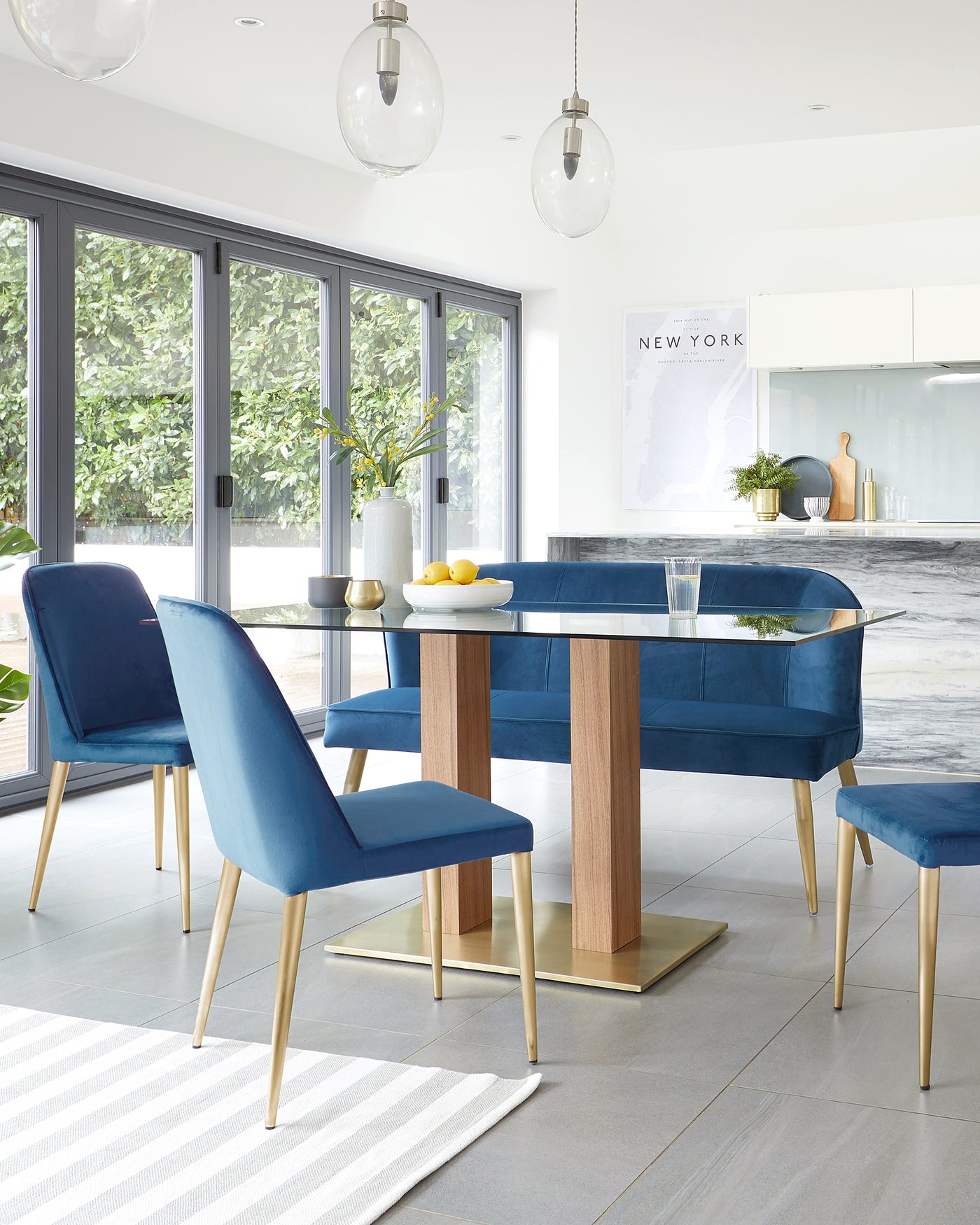 Modern dining room set featuring a rectangular table with a sleek, reflective surface, sturdy wooden legs with a natural finish, and a gold metal base plate. It is accompanied by four elegant blue upholstered chairs with cushioned seats and backs, resting on slim tapered legs with a matching gold finish. A simple yet sophisticated ensemble that exudes contemporary style.