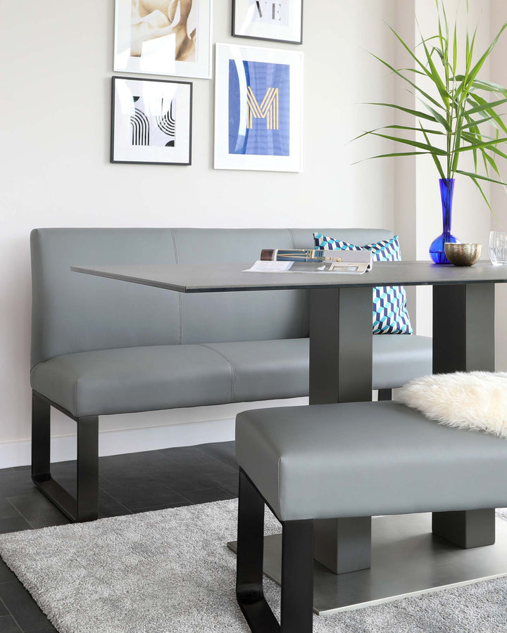 Modern minimalist furniture set including a slate grey bench with a high backrest and structural leg design, complemented by a matching square ottoman, both with a sleek faux leather finish, set against a neutral-toned room with framed abstract wall art.