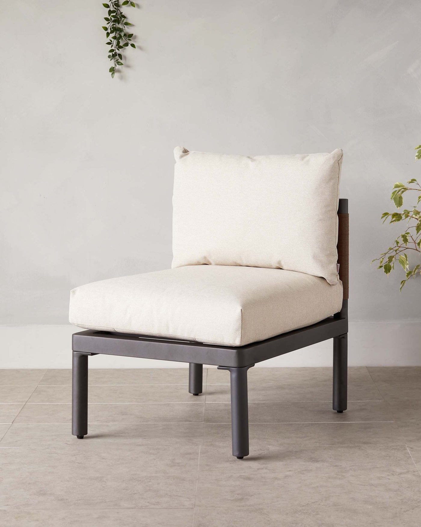 Modern minimalist armless lounge chair with a black wooden frame and off-white upholstered cushions, accompanied by a single square throw pillow on a neutral toned background with a hint of greenery.
