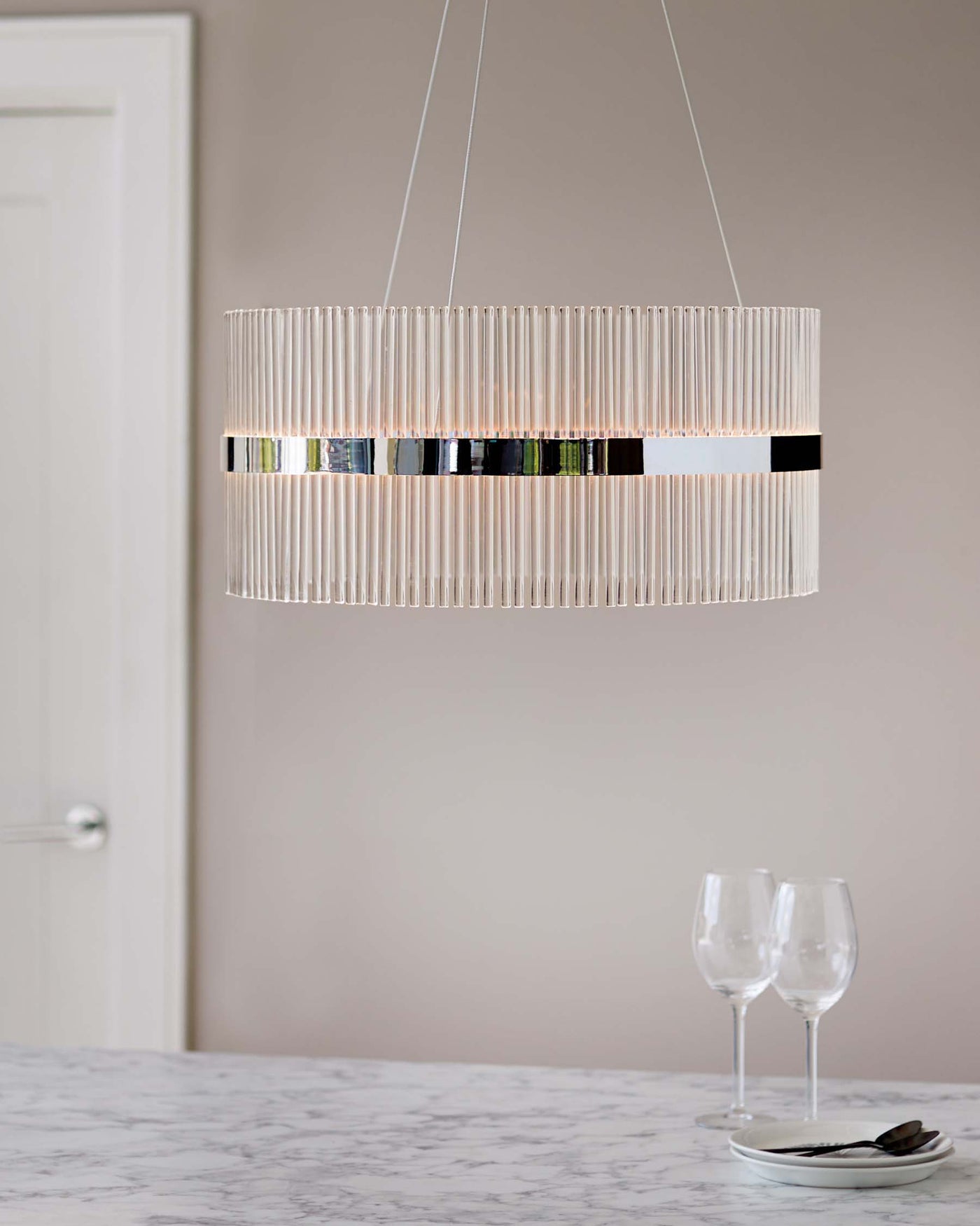Contemporary pendant light with cylindrical clear glass rods and sleek black accent band, suspended above a marble countertop displaying stemware and flatware.