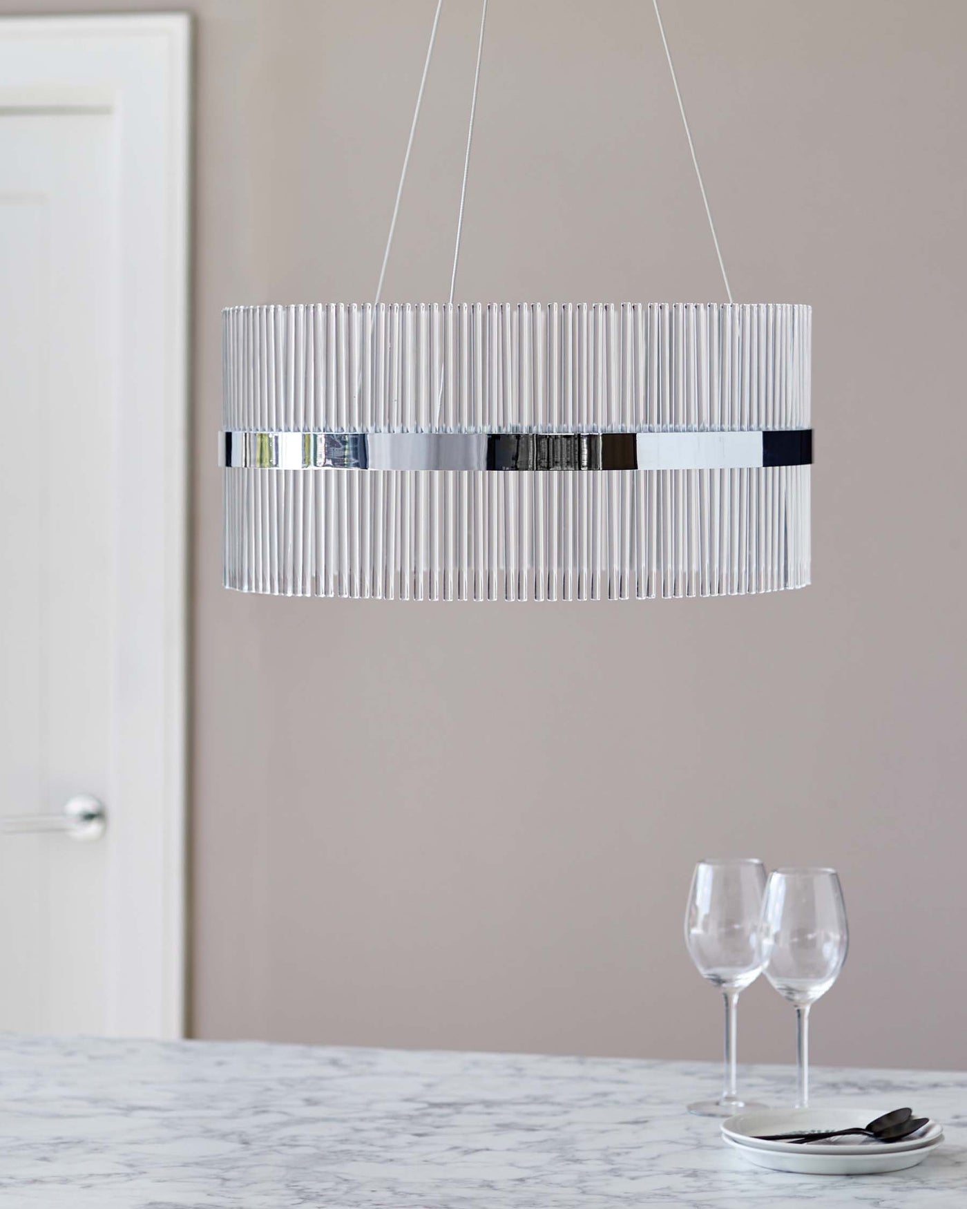 Modern cylindrical pendant light with vertical frosted glass rods and chrome accents suspended above a marble countertop.