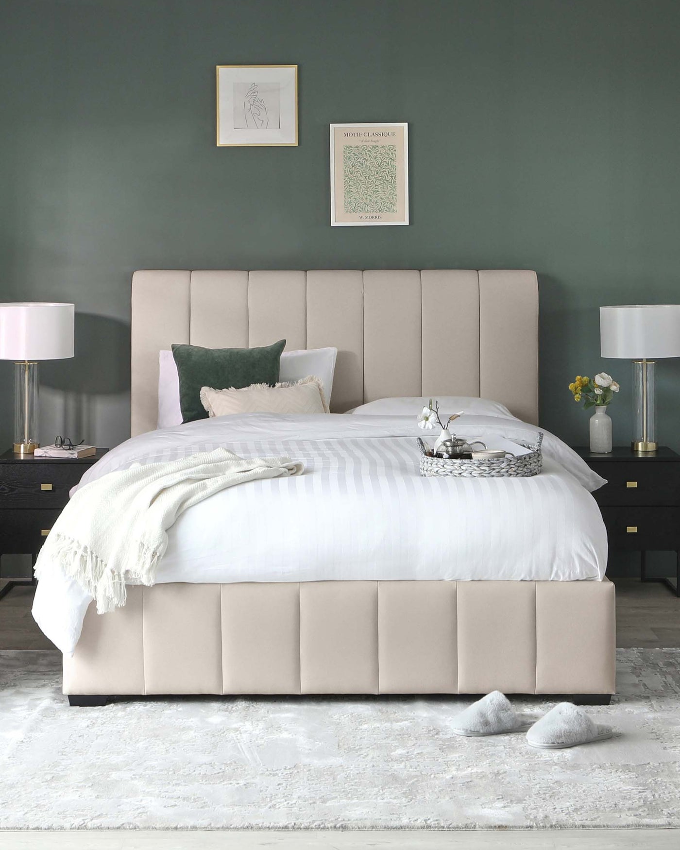 Elegant bedroom furniture setup including a large contemporary upholstered bed with a tufted headboard in a blush tone, flanked by two dark wood nightstands with gold accents, and complemented by matching modern table lamps with white shades and a clear base. The bed is dressed with crisp white strip