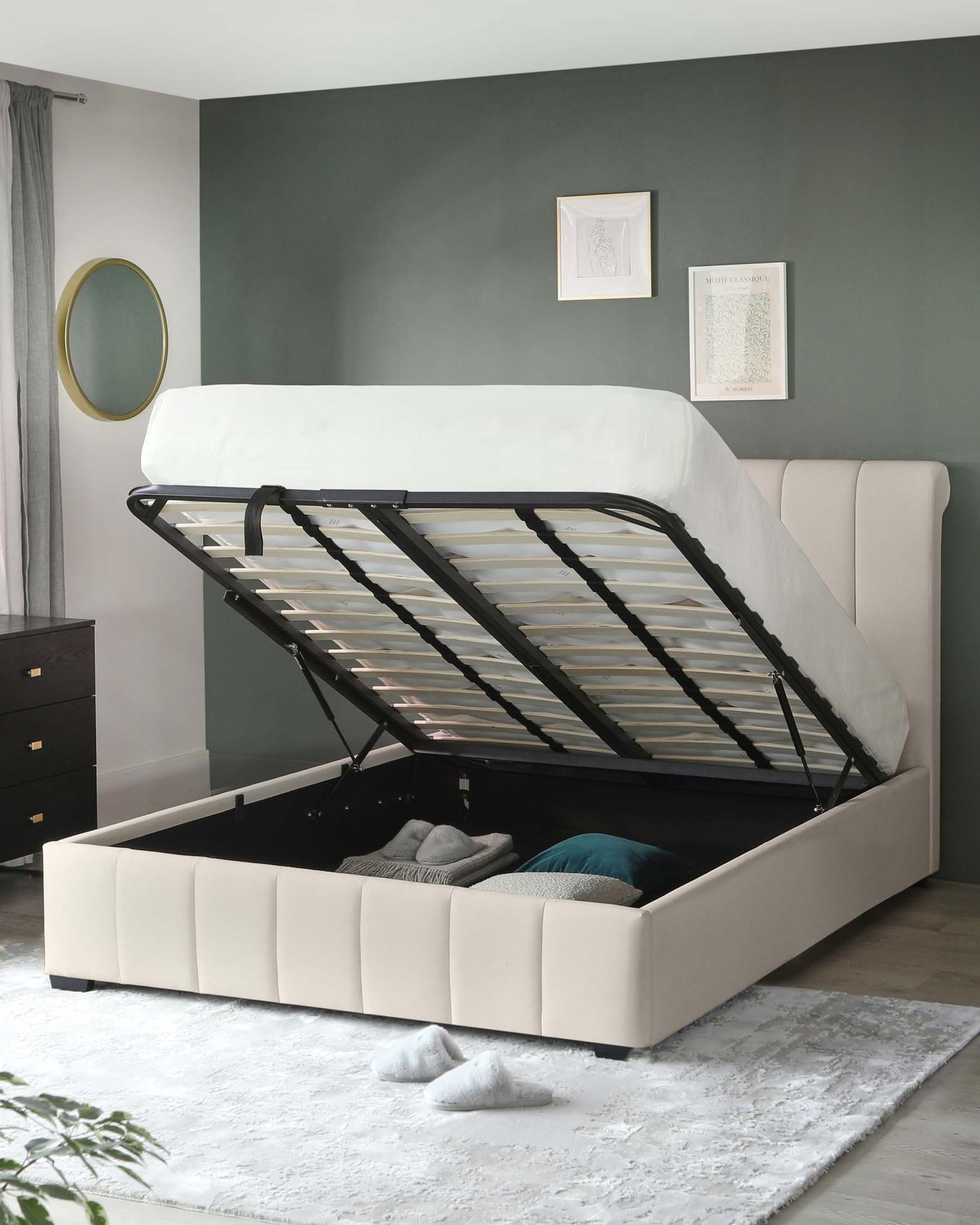 Modern upholstered storage bed with a lift-up frame revealing a spacious storage compartment, featuring a tall padded headboard and a sleek design in a neutral colour palette. A coordinating dark wood bedside drawer cabinet is also visible.