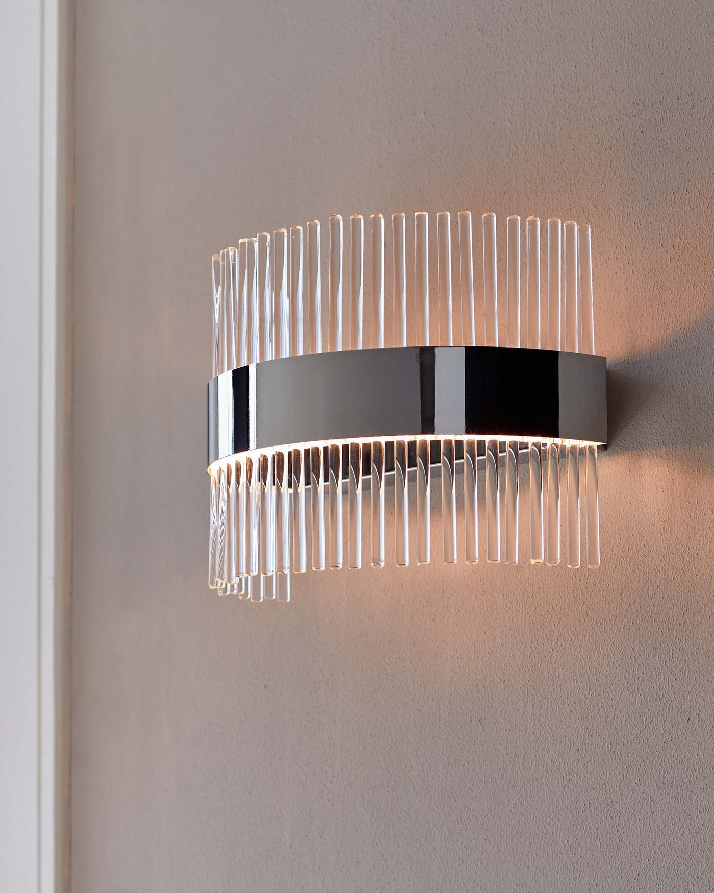 Contemporary wall-mounted light fixture with a cylindrical chrome base and vertical clear glass rods creating a radiant lighting effect on a neutral wall.