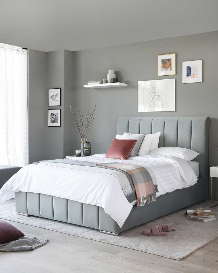 Elegant grey upholstered king-size bed with a high tufted headboard and bedding, flanked by matching white nightstands. In the background, there's a wall-mounted white shelf displaying minimalistic decor items.