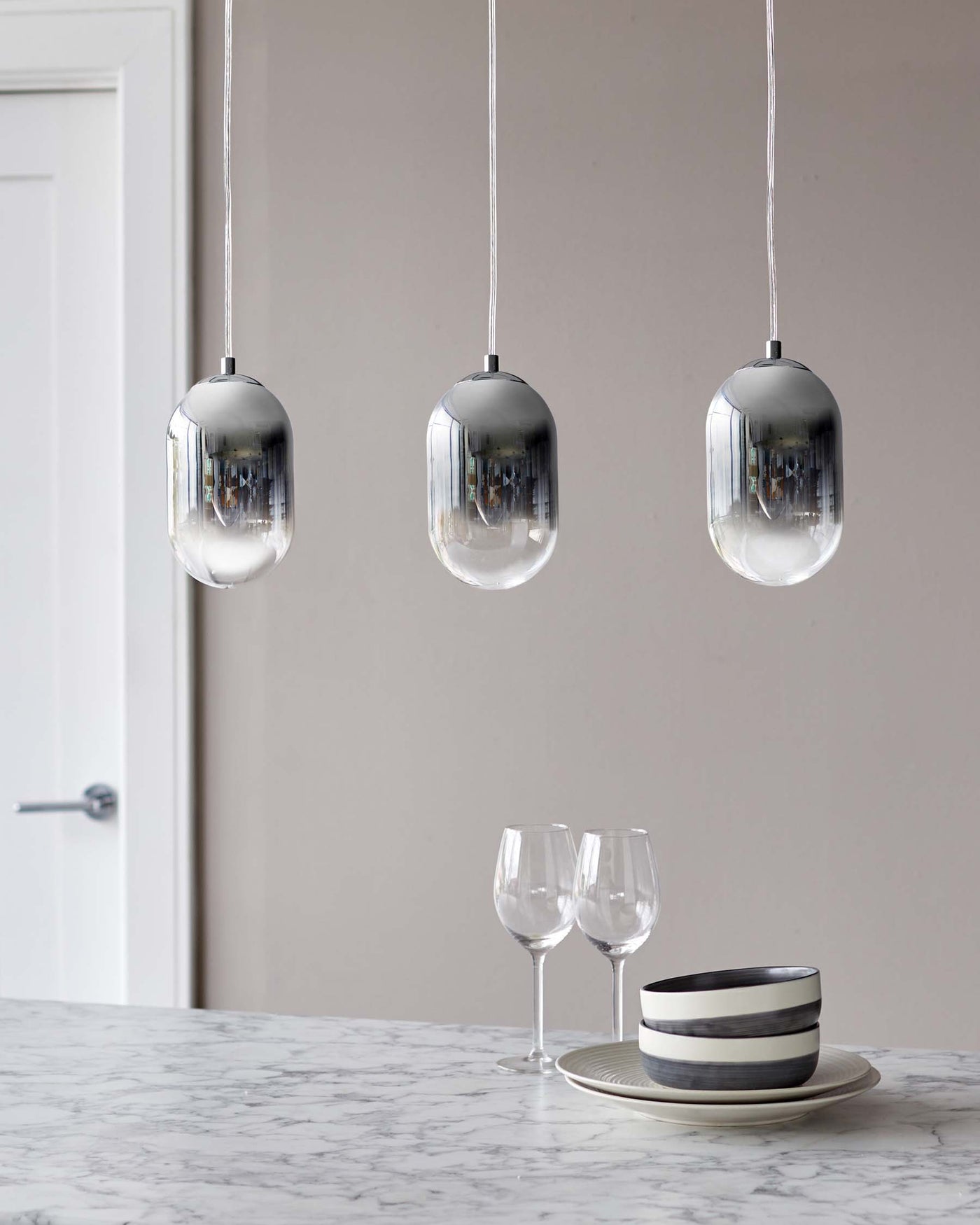 Elegant marble countertop paired with three sleek pendant lights featuring transparent glass shades and cylindrical silver tops, suspended by slender cables.