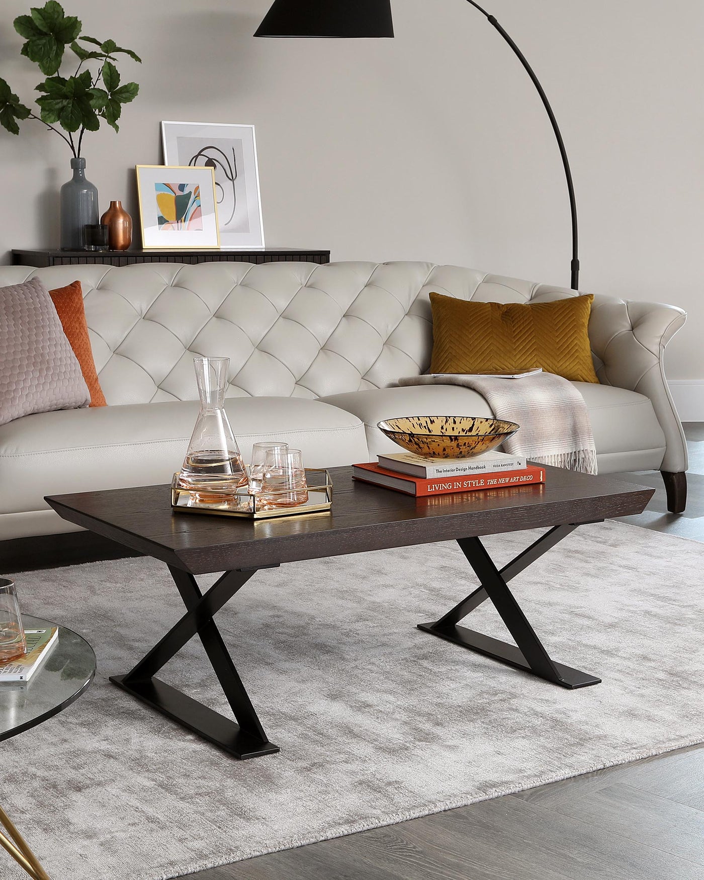 Elegant contemporary living room featuring a tufted cream leather sofa with plush cushions, accompanied by a modern dark wood coffee table with unique X-shaped metal legs, all atop a soft grey area rug.