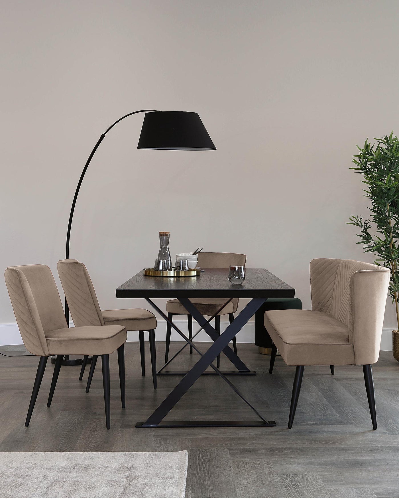 Contemporary dining room featuring a rectangular dark tabletop with unique X-shaped metallic legs, accompanied by two upholstered chairs with vertical stitch detailing and black splayed legs, and complemented by a sleek, overhanging floor lamp with an arched design and a large black shade.