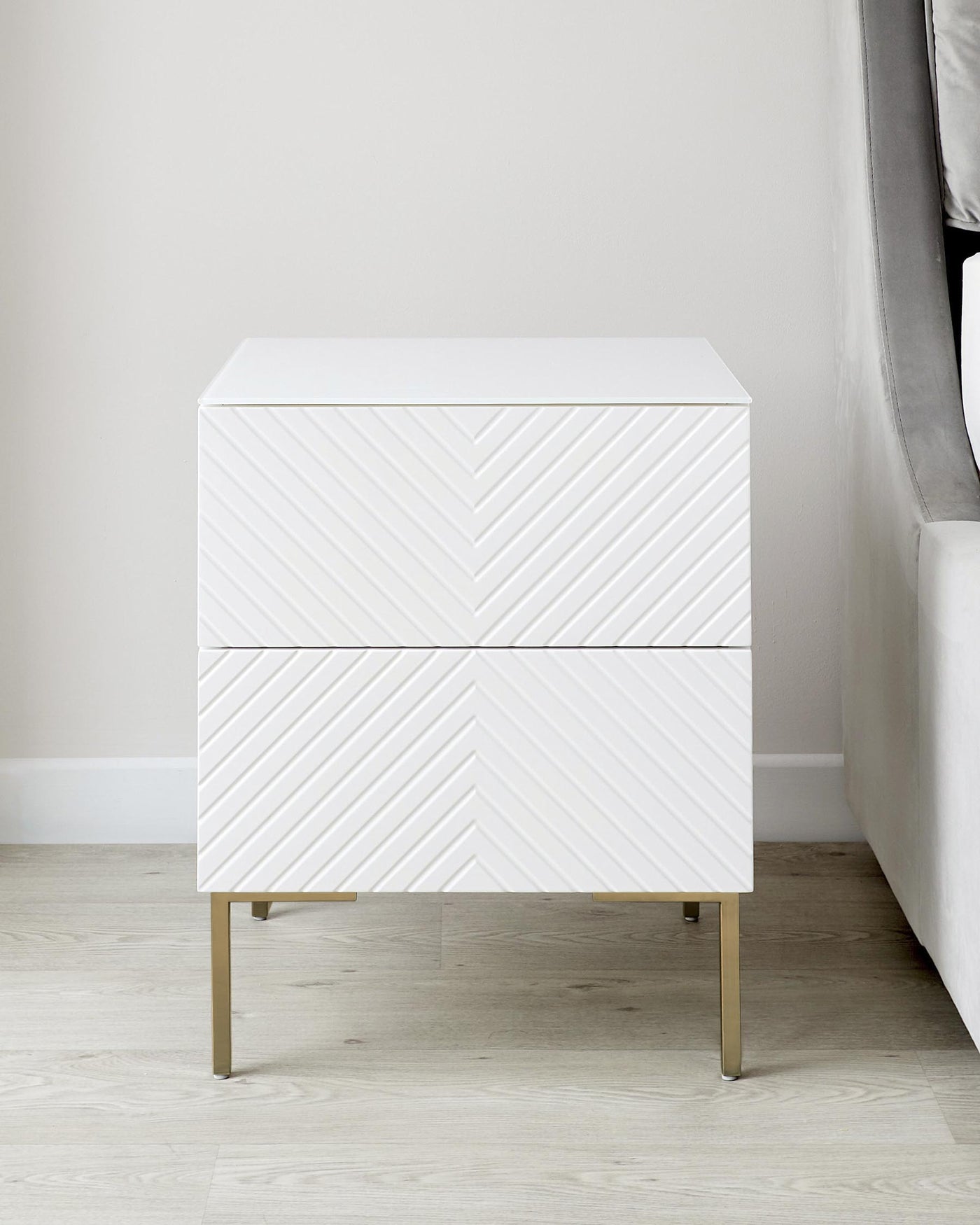 White modern two-drawer nightstand with chevron pattern and brass metal legs.