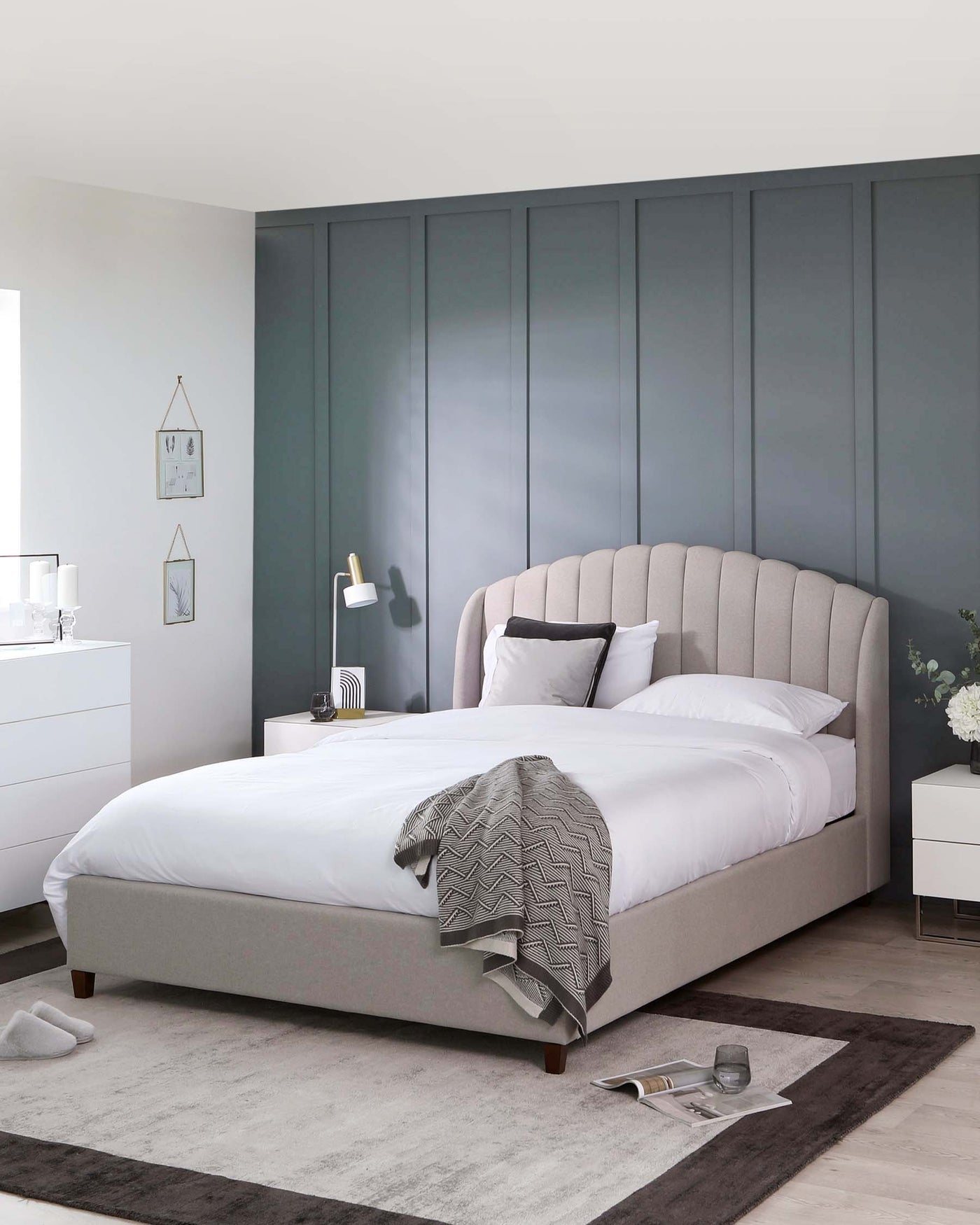 Elegant bedroom furniture set featuring a light grey upholstered bed with a curved, channel-tufted headboard and wooden feet, paired with a white two-drawer nightstand and a white six-drawer dresser. A grey area rug and tasteful room accessories complete the contemporary look.