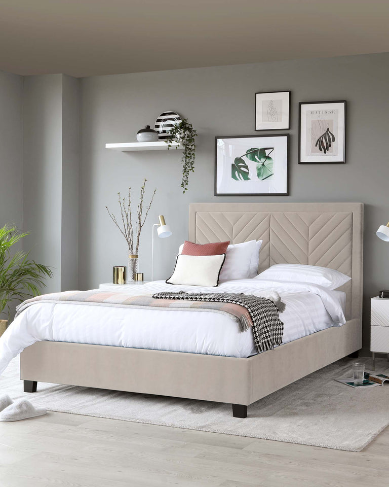 Elegant contemporary bedroom featuring an upholstered queen-size platform bed with tufted headboard in a neutral beige tone. The bed stands on dark tapered wooden legs and is dressed in white and soft pink bedding, accented with a herringbone throw. A simple white shelf mounted on the wall and a minimalist white bedside table with a drawer are seen.