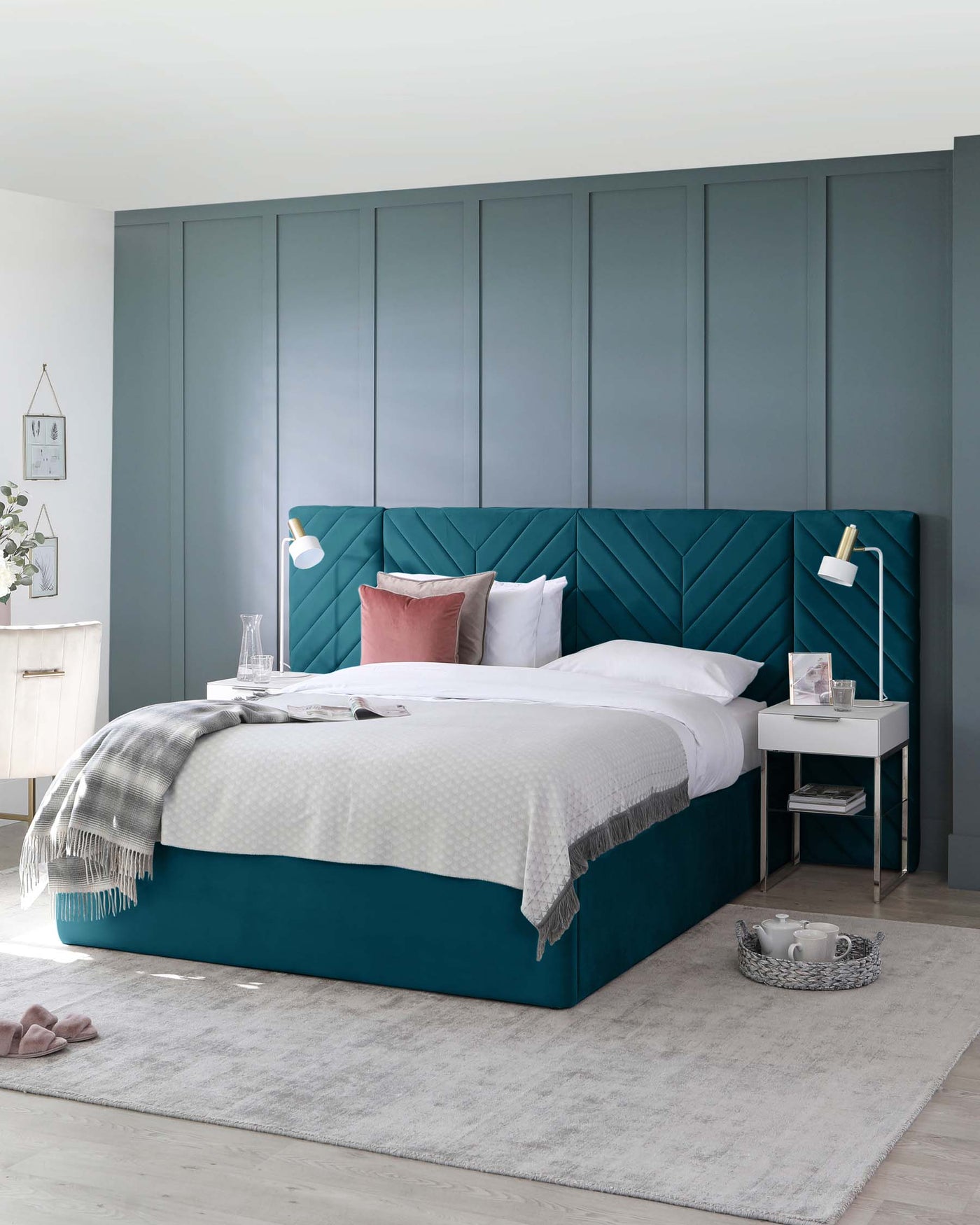 Elegant bedroom furniture featuring a large, teal, upholstered platform bed with a chevron-patterned headboard and a small, white nightstand with an open shelf and a drawer. A soft grey area rug under the bed adds to the sophisticated ambiance.
