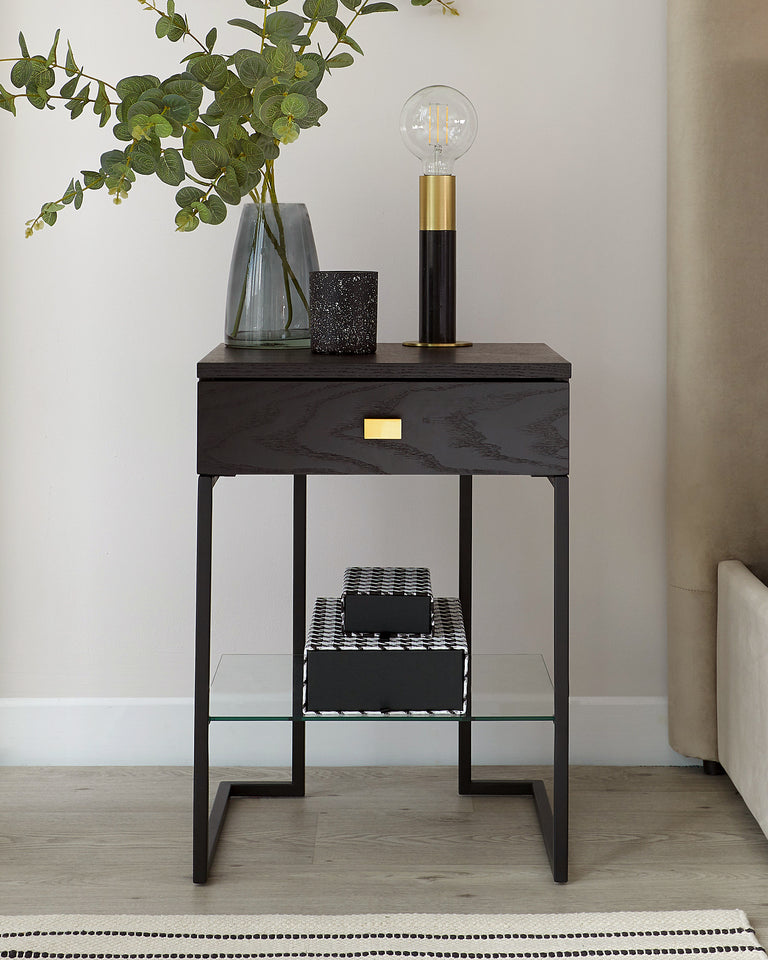 Contemporary black side table with a sleek, rectangular top and a sturdy frame featuring a lower shelf with a clear glass surface. The table has minimalist gold handles for a touch of elegance.