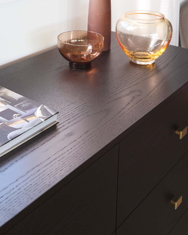 A contemporary, dark-wood sideboard with a textured finish and elegant brass handles on its drawers.