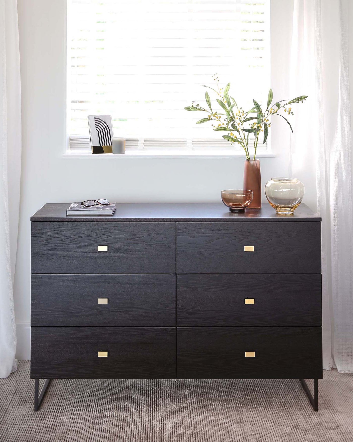 Modern black wooden sideboard with six drawers featuring brass square pulls, resting on slender metal legs.