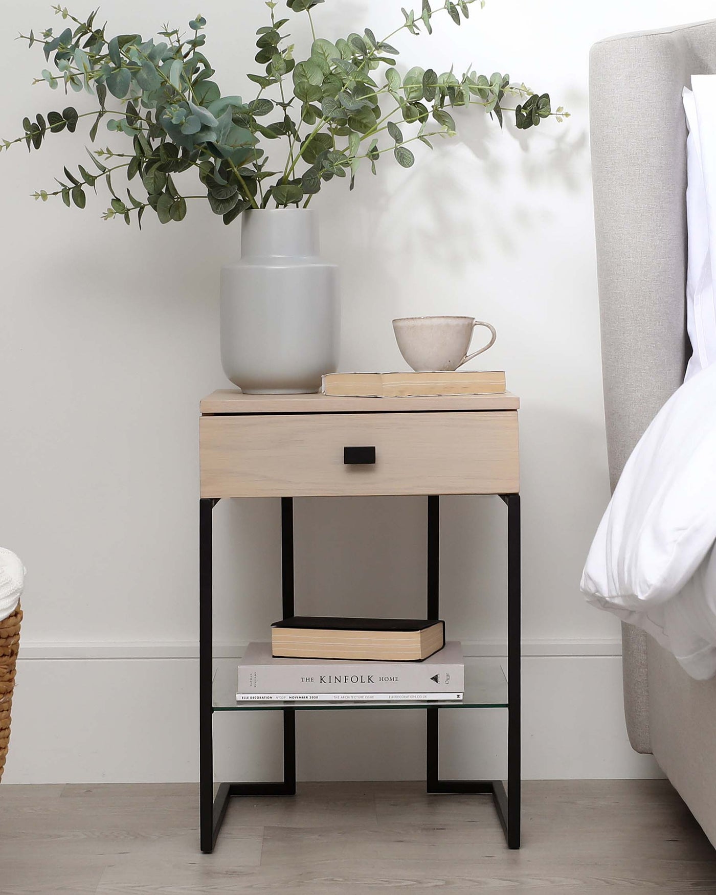 Modern minimalist bedside table with a light wood finish, a single drawer featuring a black pull handle, and a lower shelf supported by a sleek black metal frame.