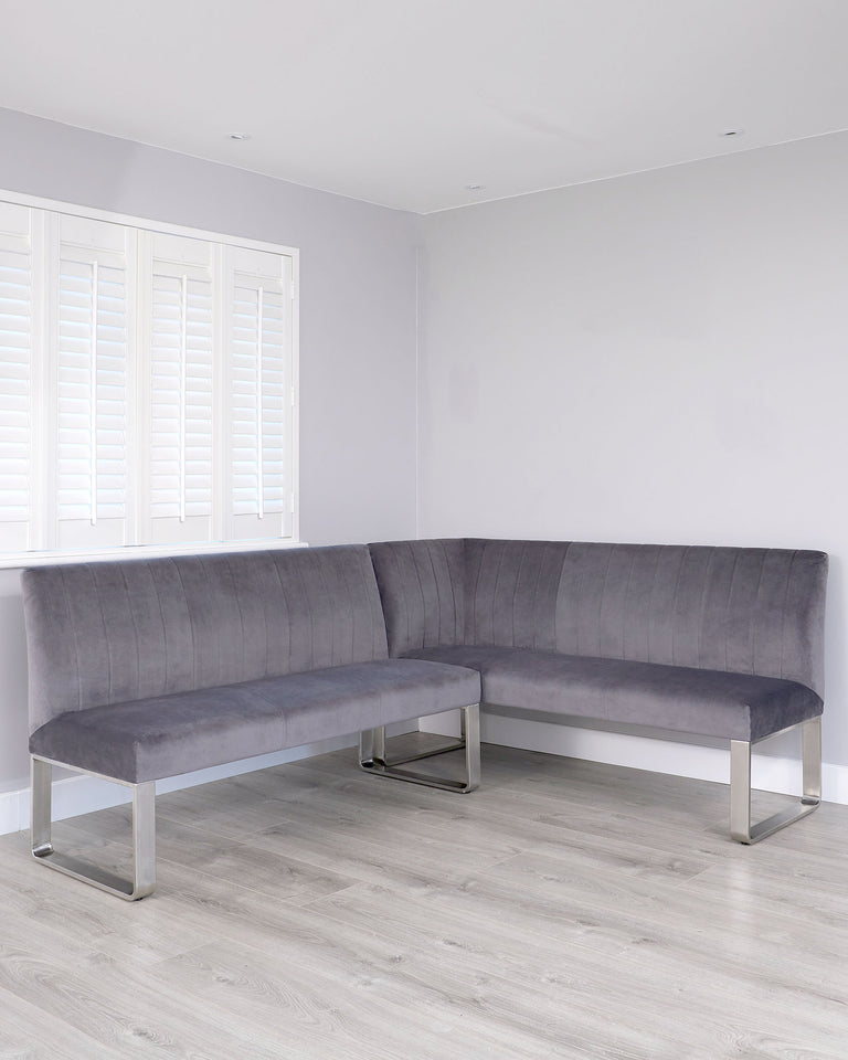 Modern L-shaped grey fabric corner sofa with clean lines and metal legs, set in a minimalist room with white plantation shutters and light wood flooring.