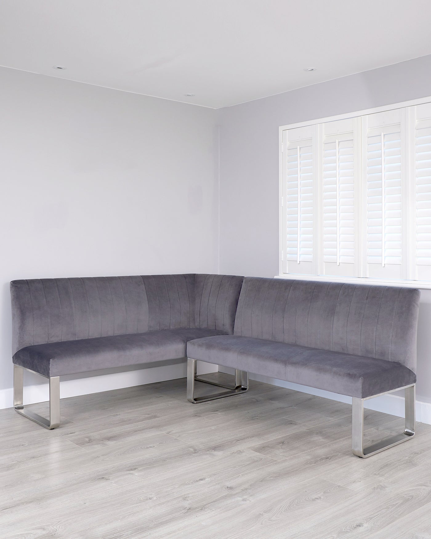 L-shaped modern corner bench with grey upholstery and sleek, chrome-finished metal legs.