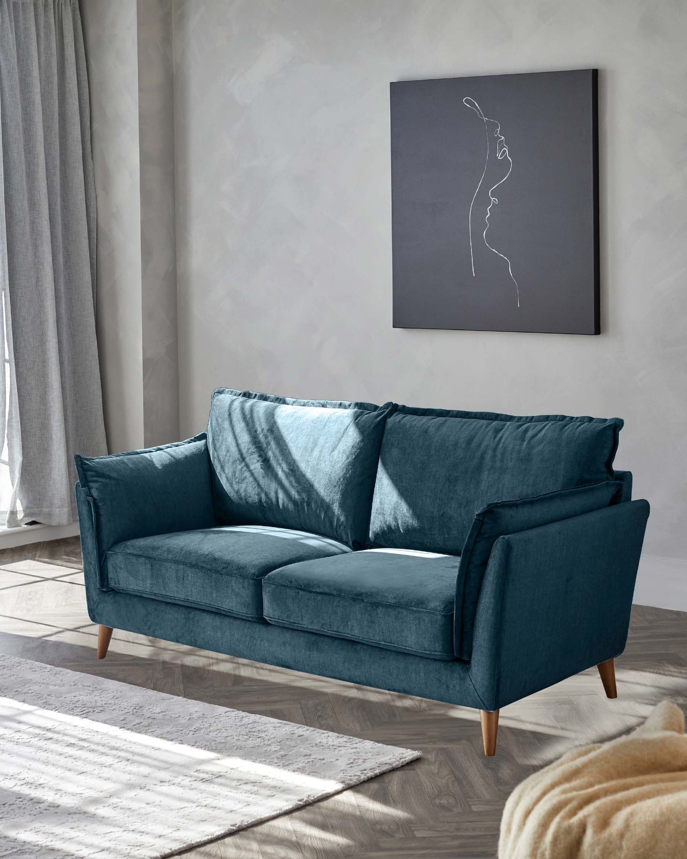 Elegant three-seater sofa in a deep teal blue velvet fabric, featuring plush cushions and a clean silhouette with square armrests. The couch stands on four tapered wooden legs and is complemented by two matching velvet throw pillows.