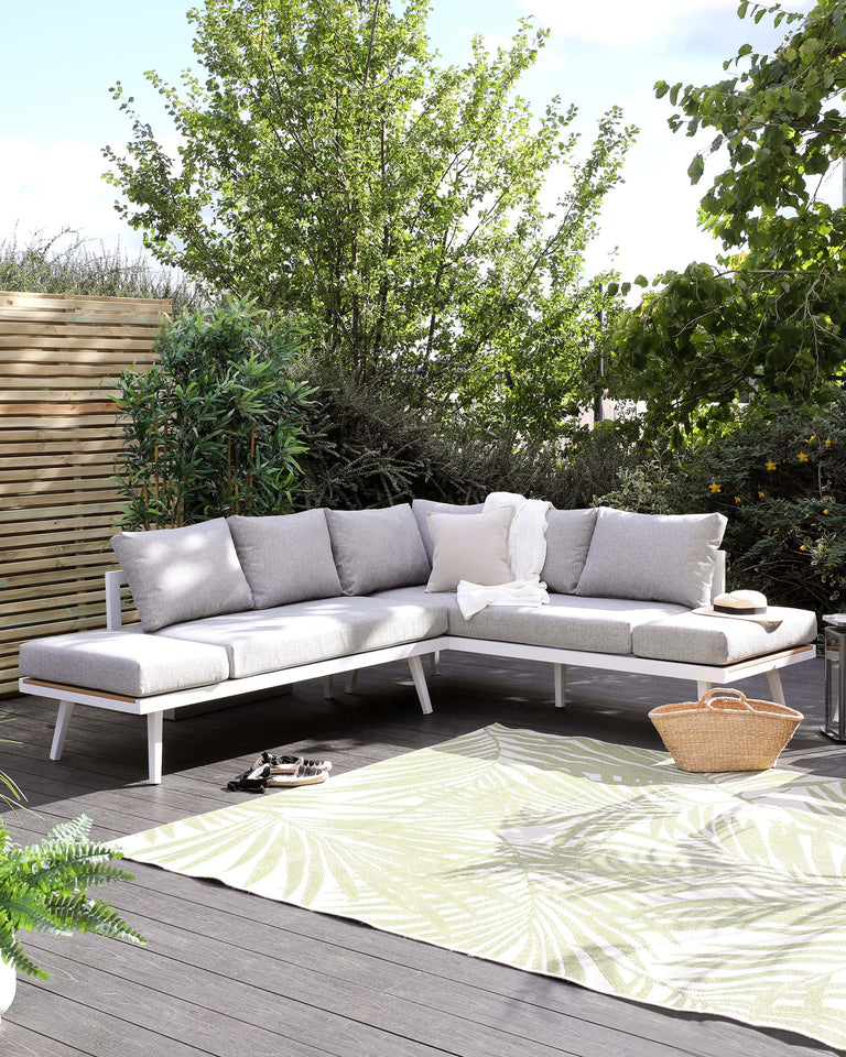 Modern outdoor sectional sofa with light grey cushions on a white frame, accompanied by a matching white coffee table, set on a dark wood deck with a decorative green and white area rug.