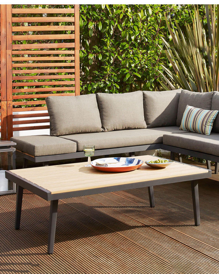 A modern outdoor furniture set featuring a sectional corner sofa with plush grey cushions and a rectangular coffee table with a light wood finish and grey metal frame. The setting suggests a comfortable and stylish patio arrangement.
