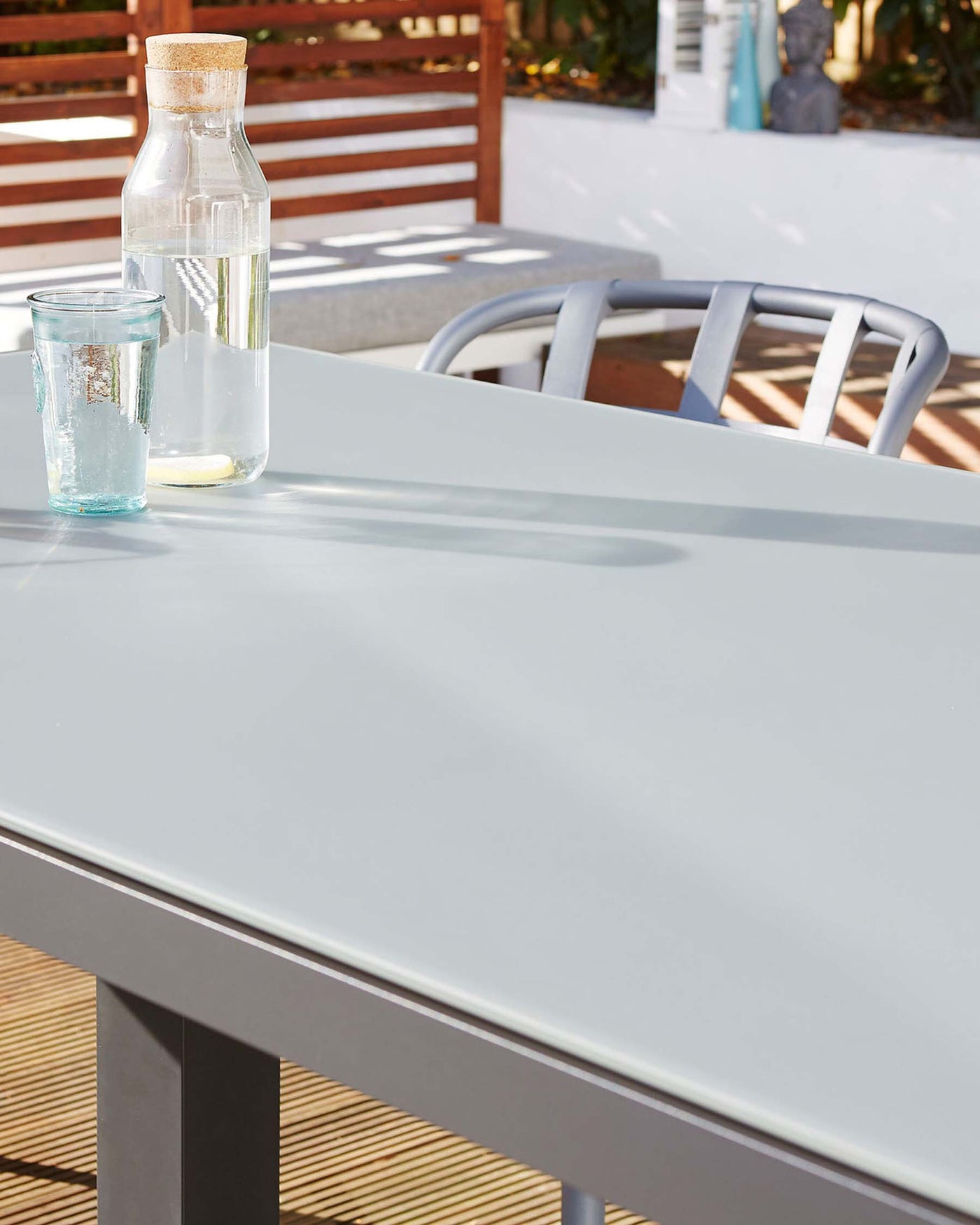 Modern outdoor furniture featuring a sleek, white rectangular table with clean lines and a smooth finish, accompanied by a stylish grey aluminium chair with a minimalist curved backrest.