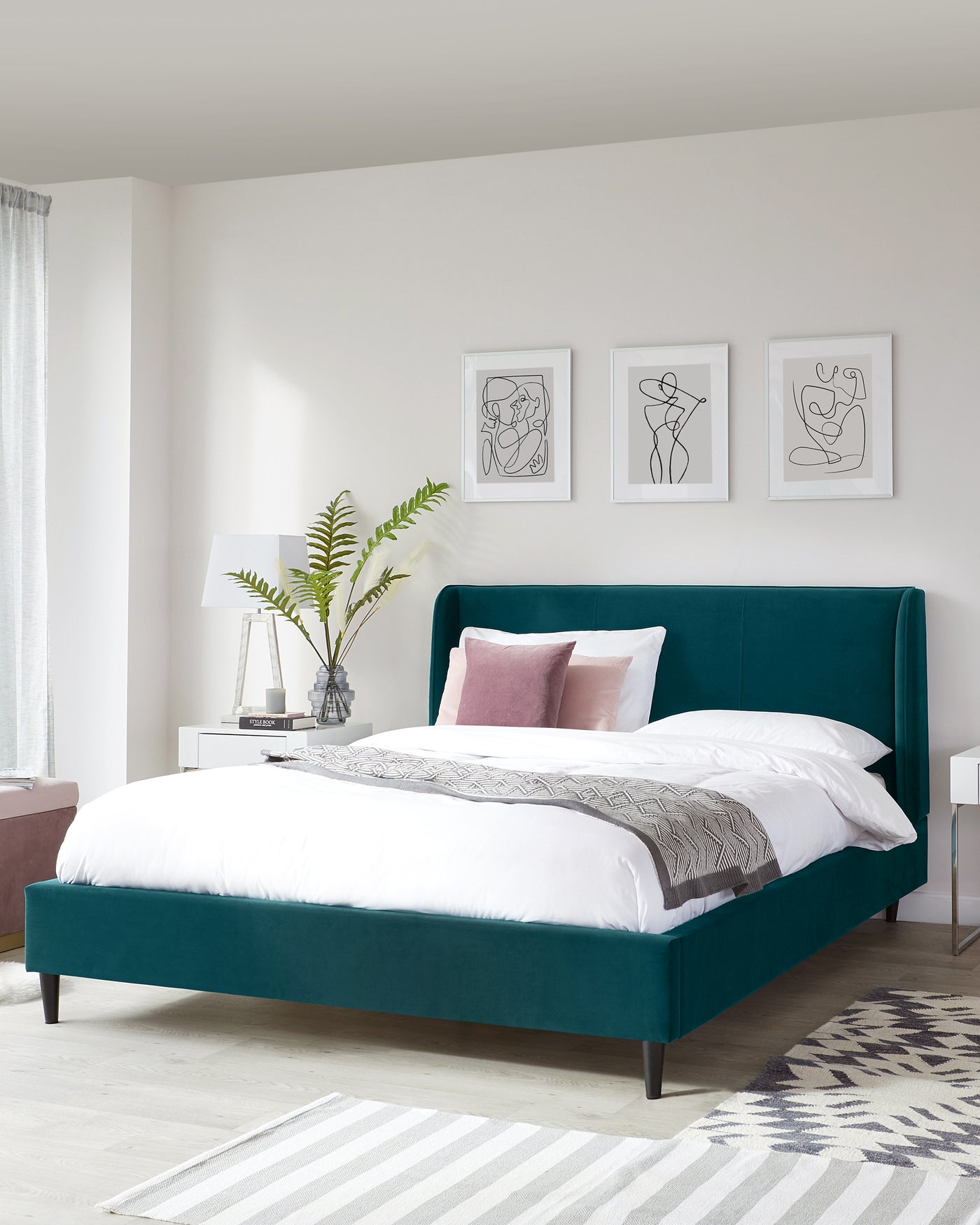 Elegant teal upholstered bed with a high, straight-lined headboard and low-profile design, paired with a simple white nightstand.