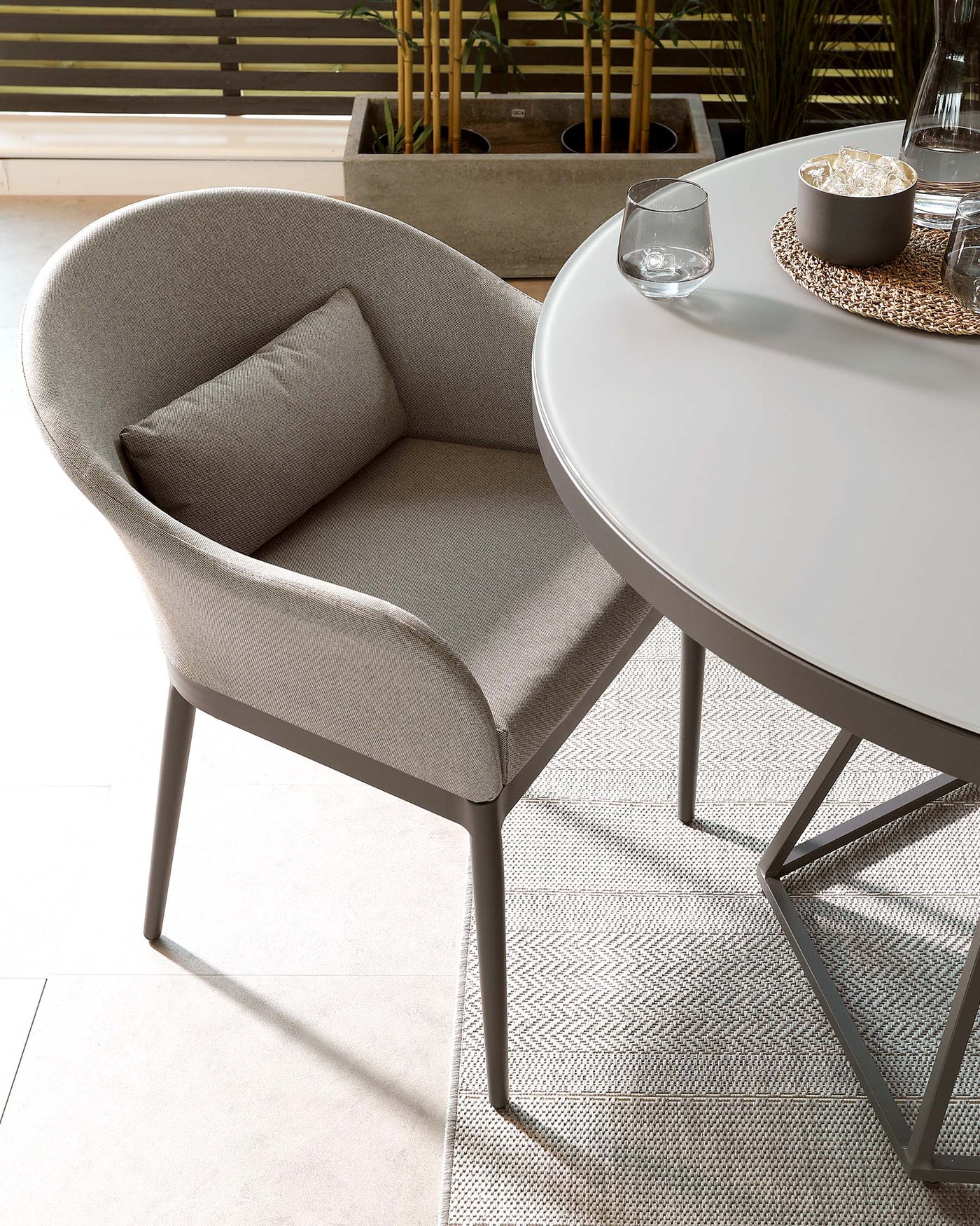 Modern, round white dining table with sleek, grey metal legs paired with a contemporary light grey upholstered chair featuring a curved backrest, cushioned seat, and square metal legs.