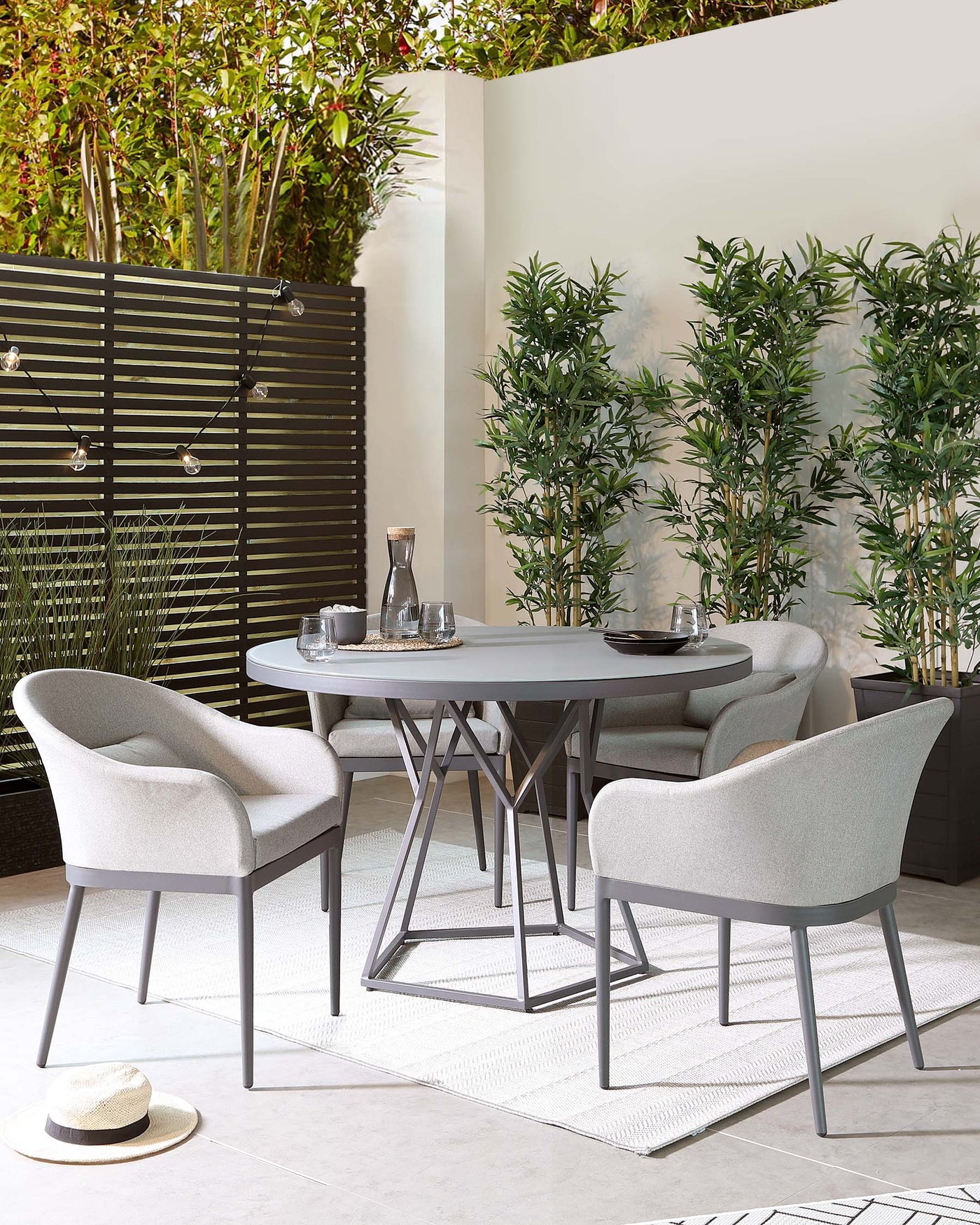 Modern outdoor dining set featuring a round, grey tabletop with a geometric metal base and four comfortable armchairs upholstered in light grey fabric with sleek metal legs.