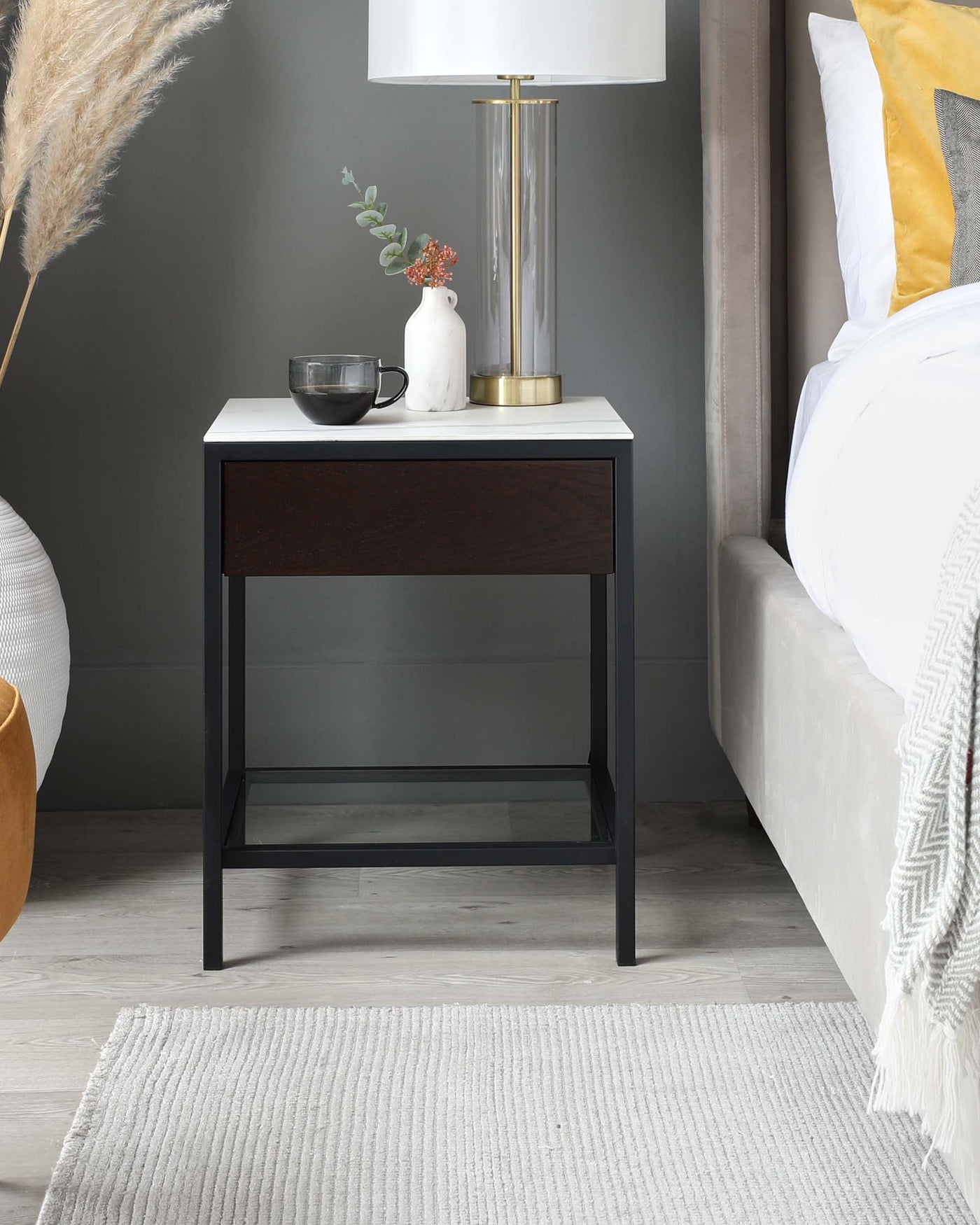 Modern minimalist bedside table with a sleek design featuring a white tabletop and a dark wooden drawer on a black metal frame, complemented by an open lower shelf providing additional storage space. Perfect for contemporary bedroom decor.