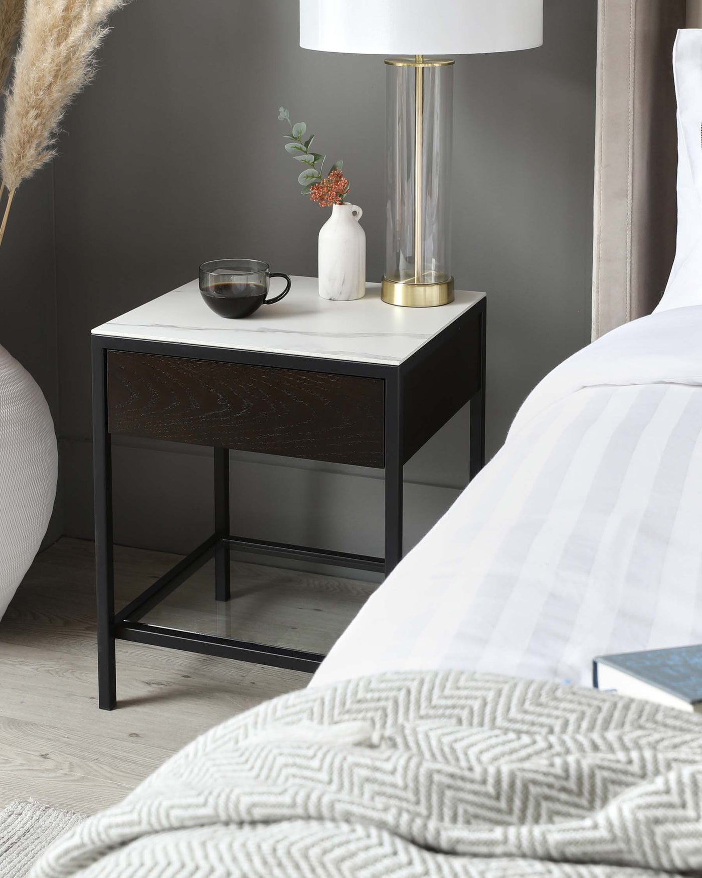 A modern bedside table with a black metal frame and a white marble top, featuring a single drawer with a dark wood front.