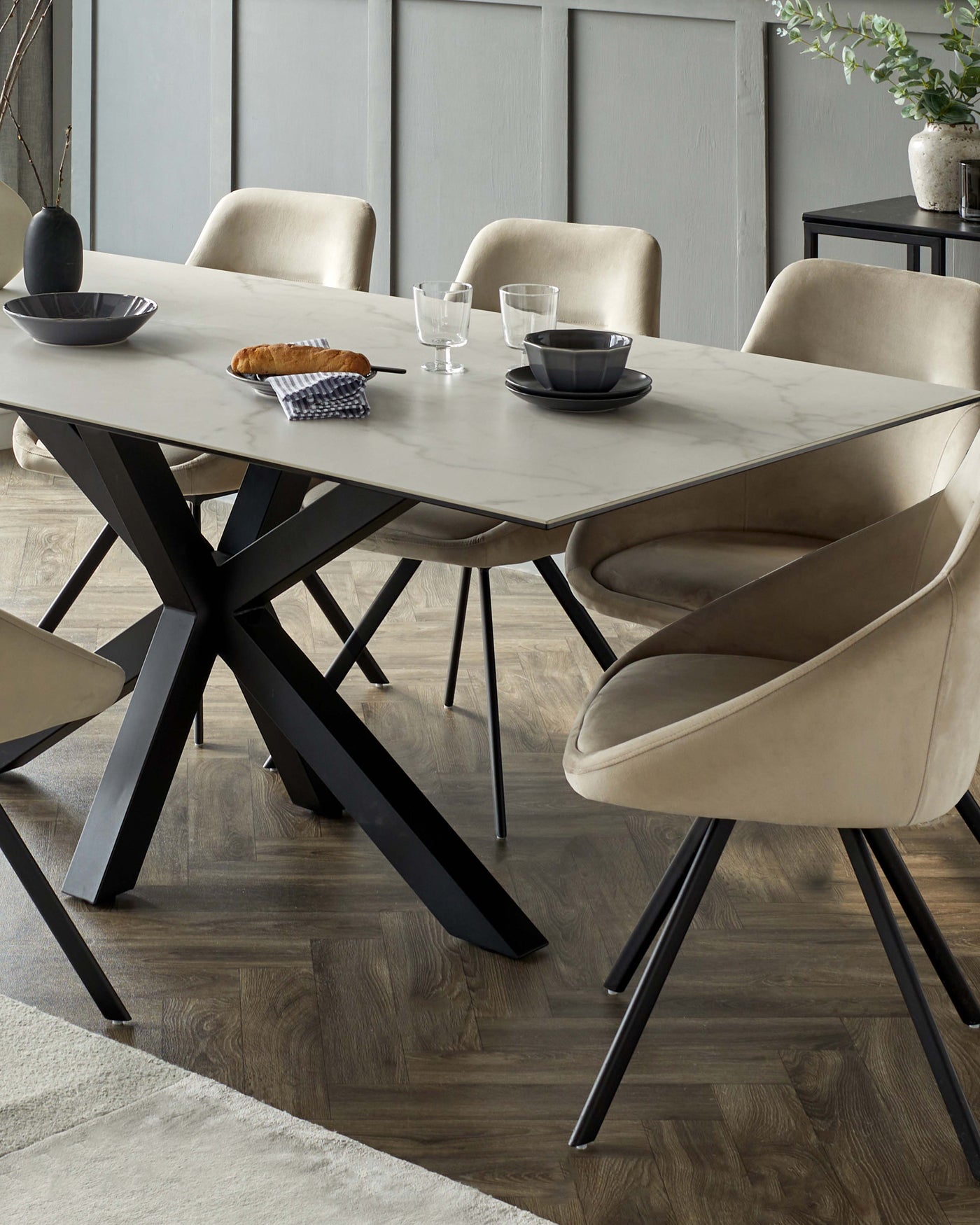 Contemporary dining room featuring a rectangular marble-top table with a unique geometric black metal base and a set of luxurious beige velvet upholstered chairs with metal legs.