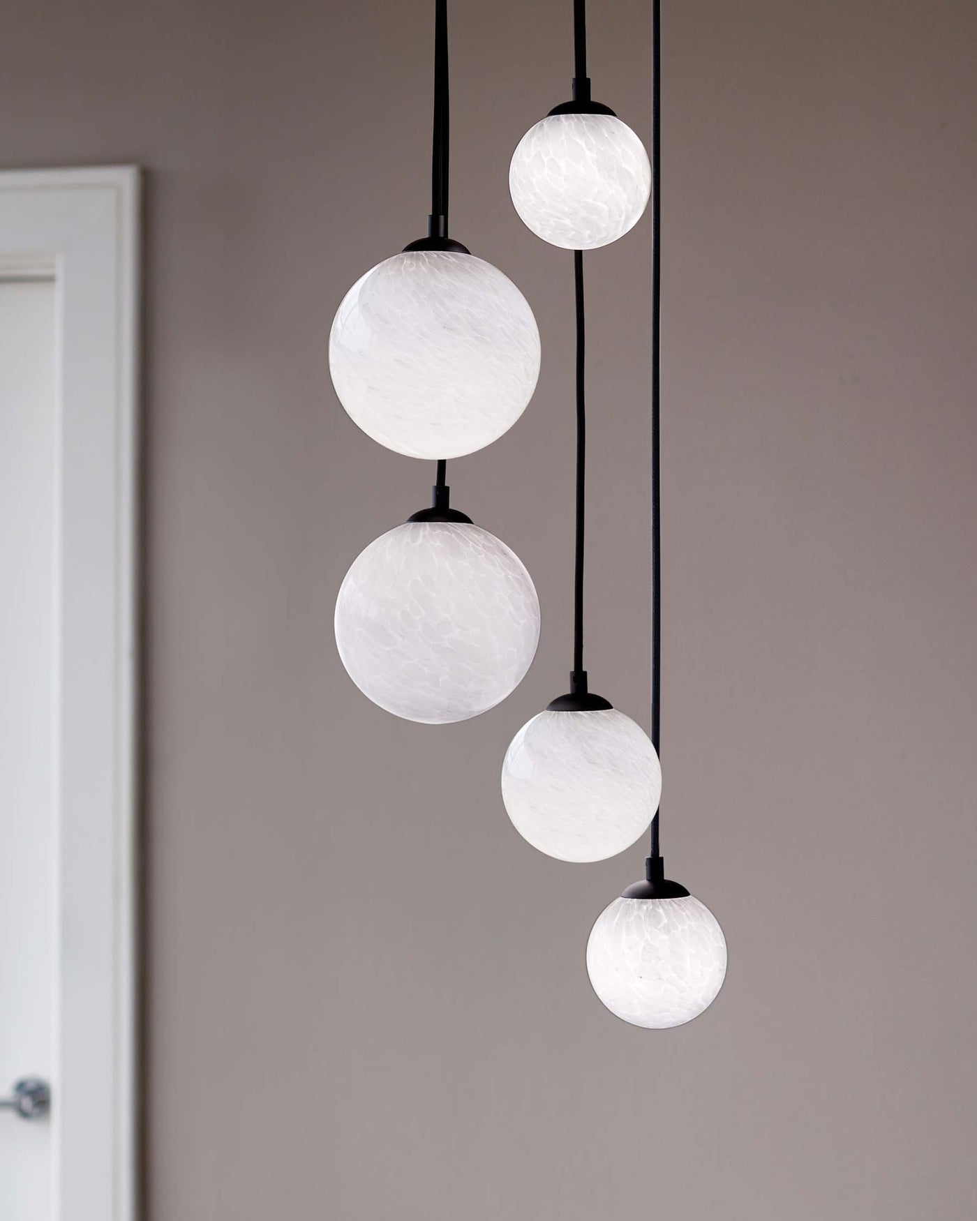 A modern pendant light fixture with five spherical white frosted glass shades of varying sizes, each suspended by a simple black cord, creating an elegant vertical cascade of ambient lighting.