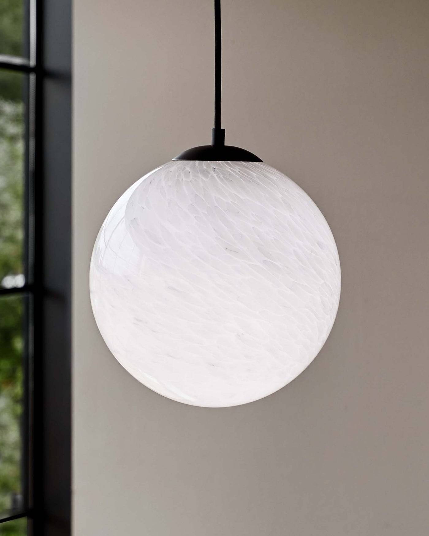 A modern spherical pendant light with a textured white glass shade and a matte black canopy, suspended from a simple black cord against a neutral background.