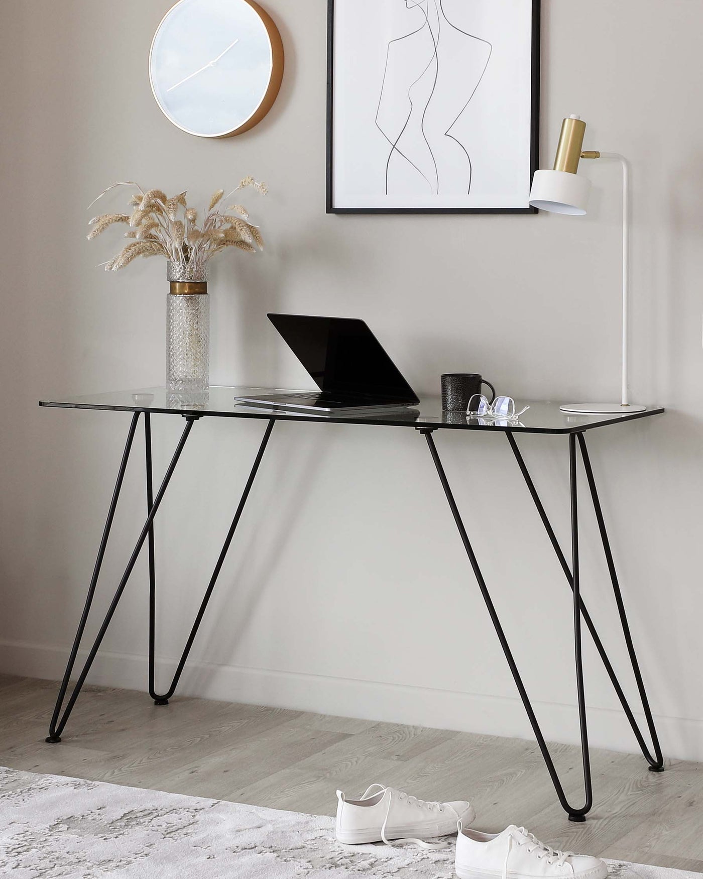 A modern minimalist black metal frame desk with a glass top, featuring sleek, angled legs.