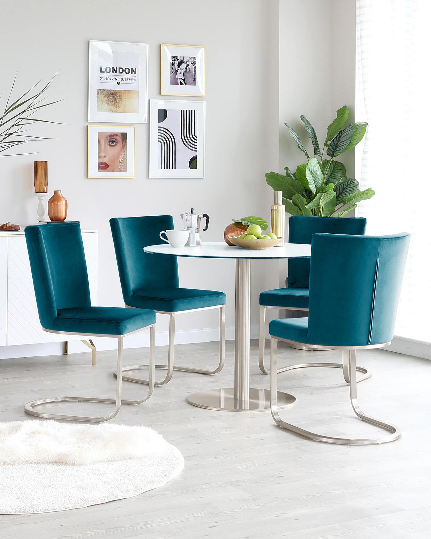A modern dining set featuring a round, white tabletop with a reflective chrome pedestal base, accompanied by four luxurious teal velvet upholstered chairs with sleek chrome cantilever bases.