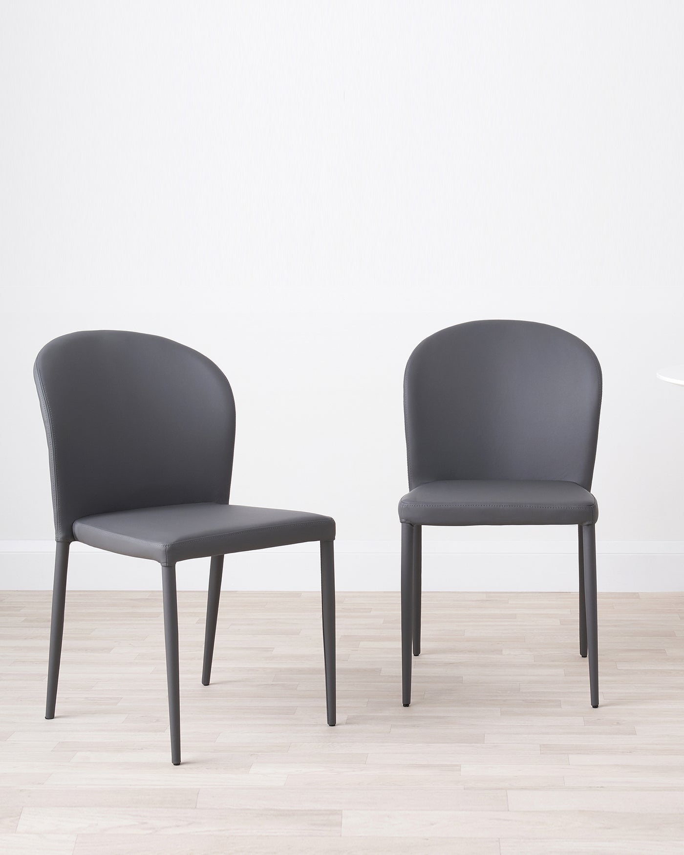 Two modern grey upholstered dining chairs with sleek black metal legs, set on a light hardwood floor against a plain white wall.
