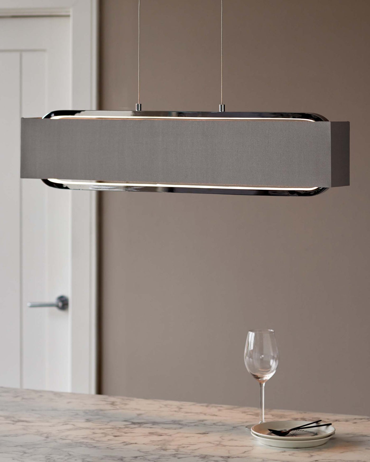 Contemporary rectangular pendant light with a grey fabric shade and polished chrome accents hanging above a marble countertop.